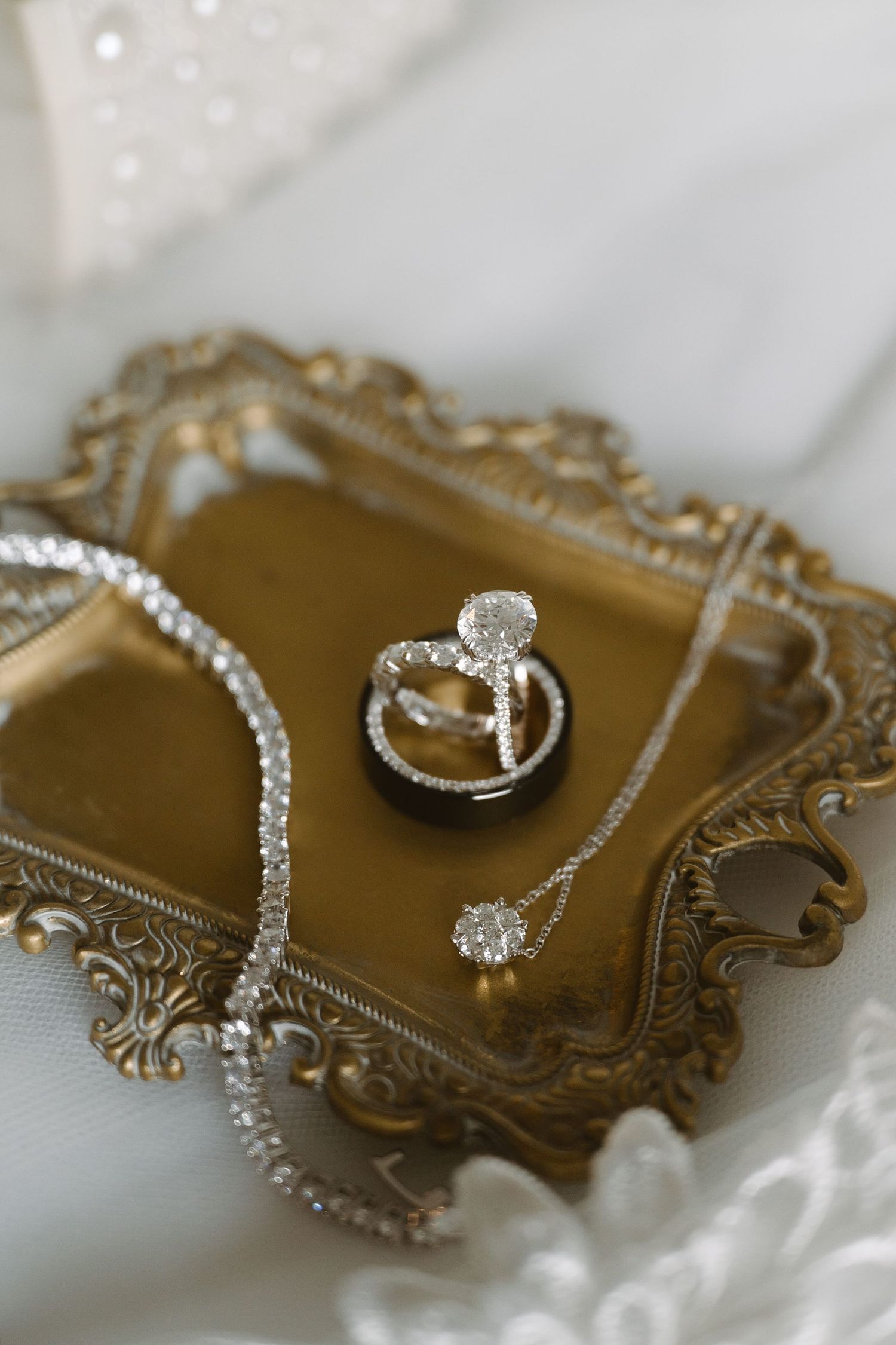 Elegant wedding rings and diamond necklace displayed on an ornate gold vintage tray with lace backdrop.
