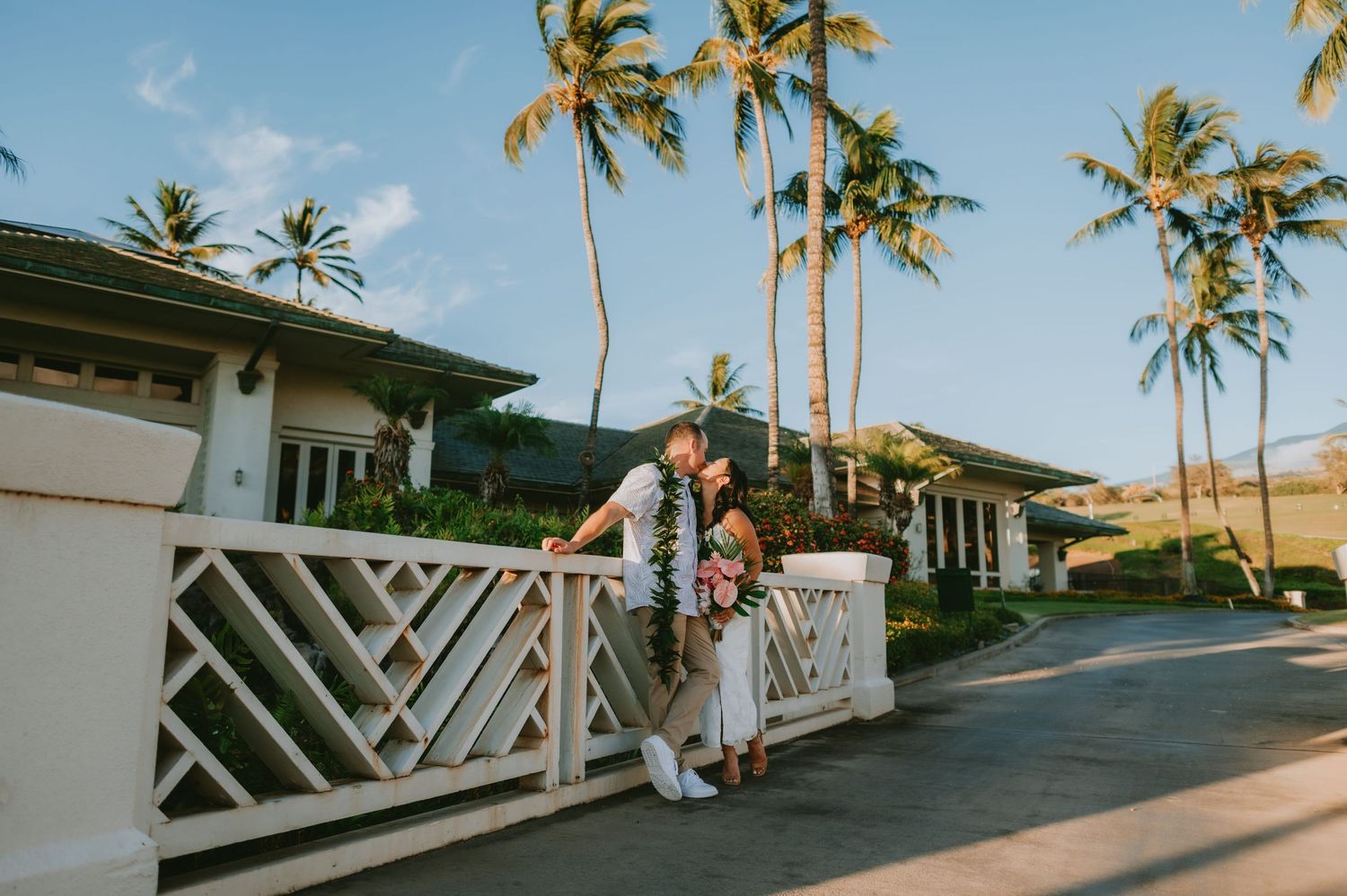 Couple sharing a romantic kiss on a white lattice bridge surrounded by tropical palm trees at a Hawaiian resort.