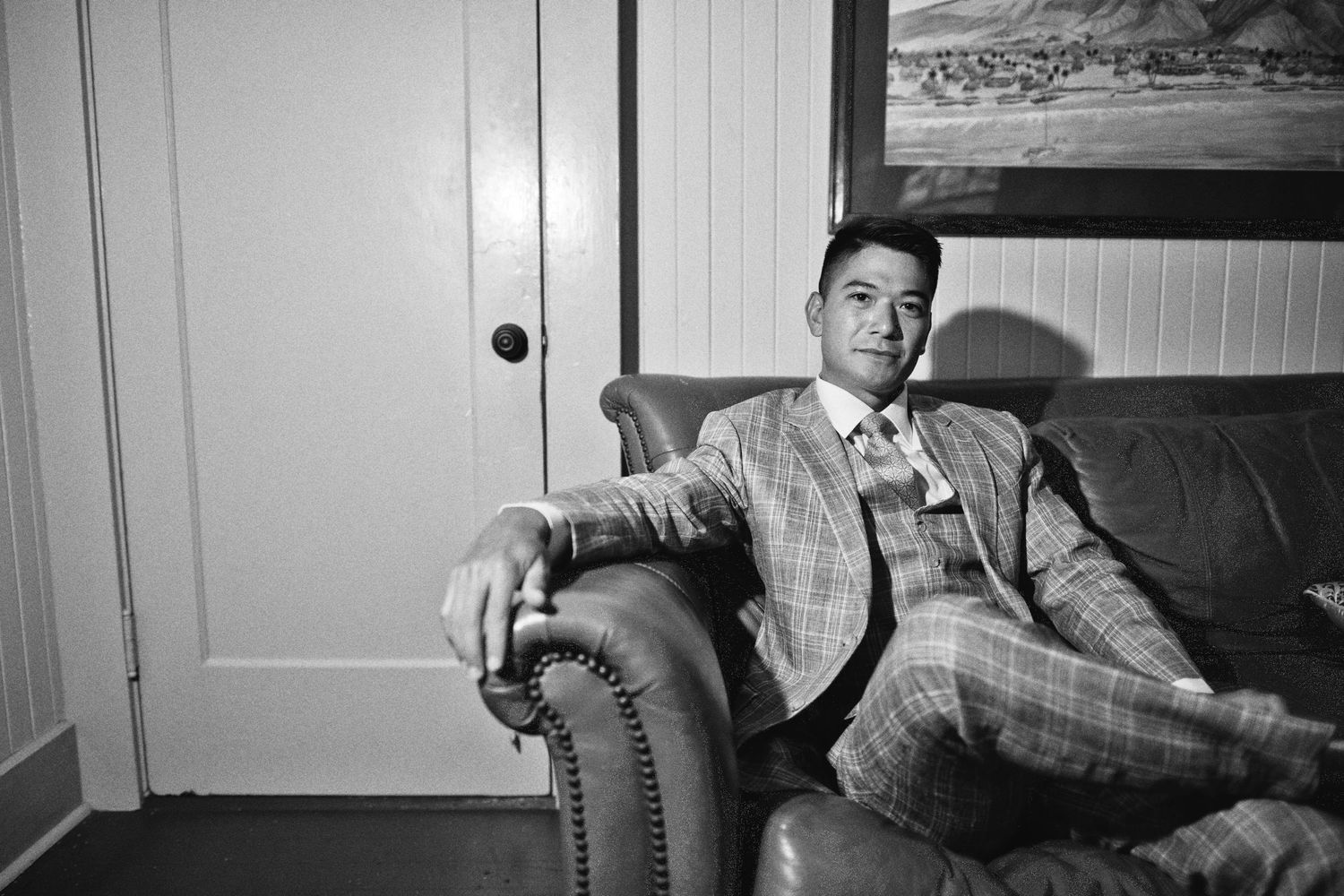 Man in plaid suit relaxing in leather armchair, black and white portrait photography.
