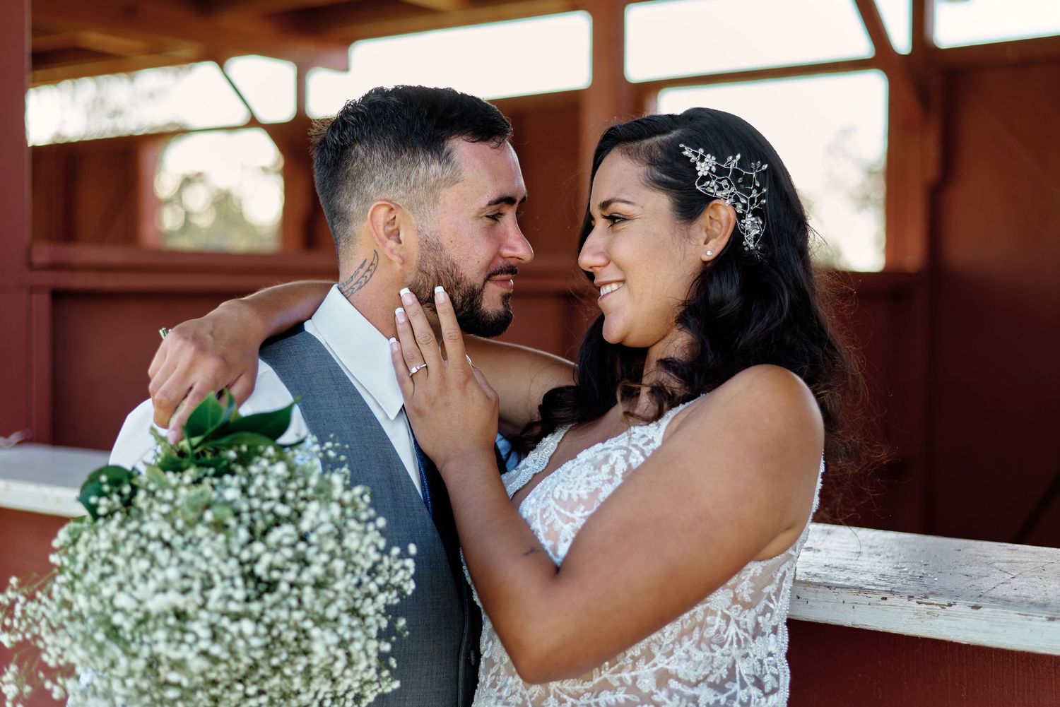 Romantic moment between newlyweds holding baby's breath bouquet in rustic venue.