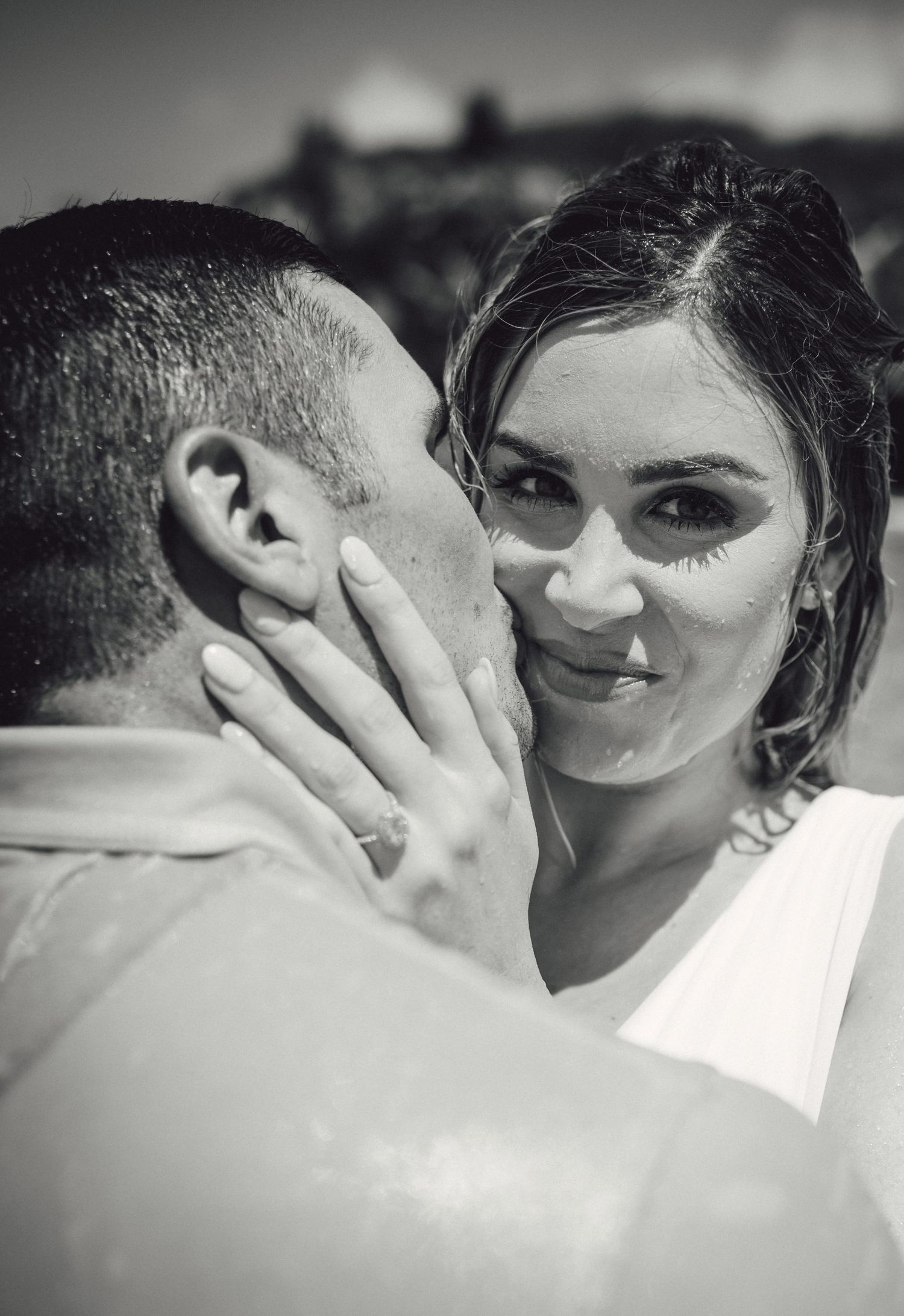 Black and white close-up of bride smiling at groom during romantic beach wedding shoot.