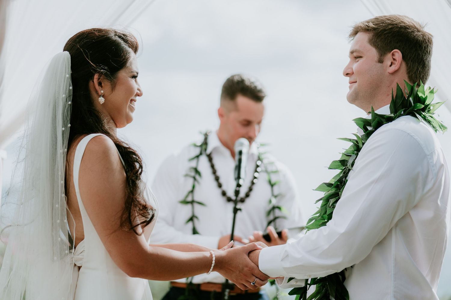 A couple exchanges vows during their outdoor wedding ceremony under a decorated white arch.