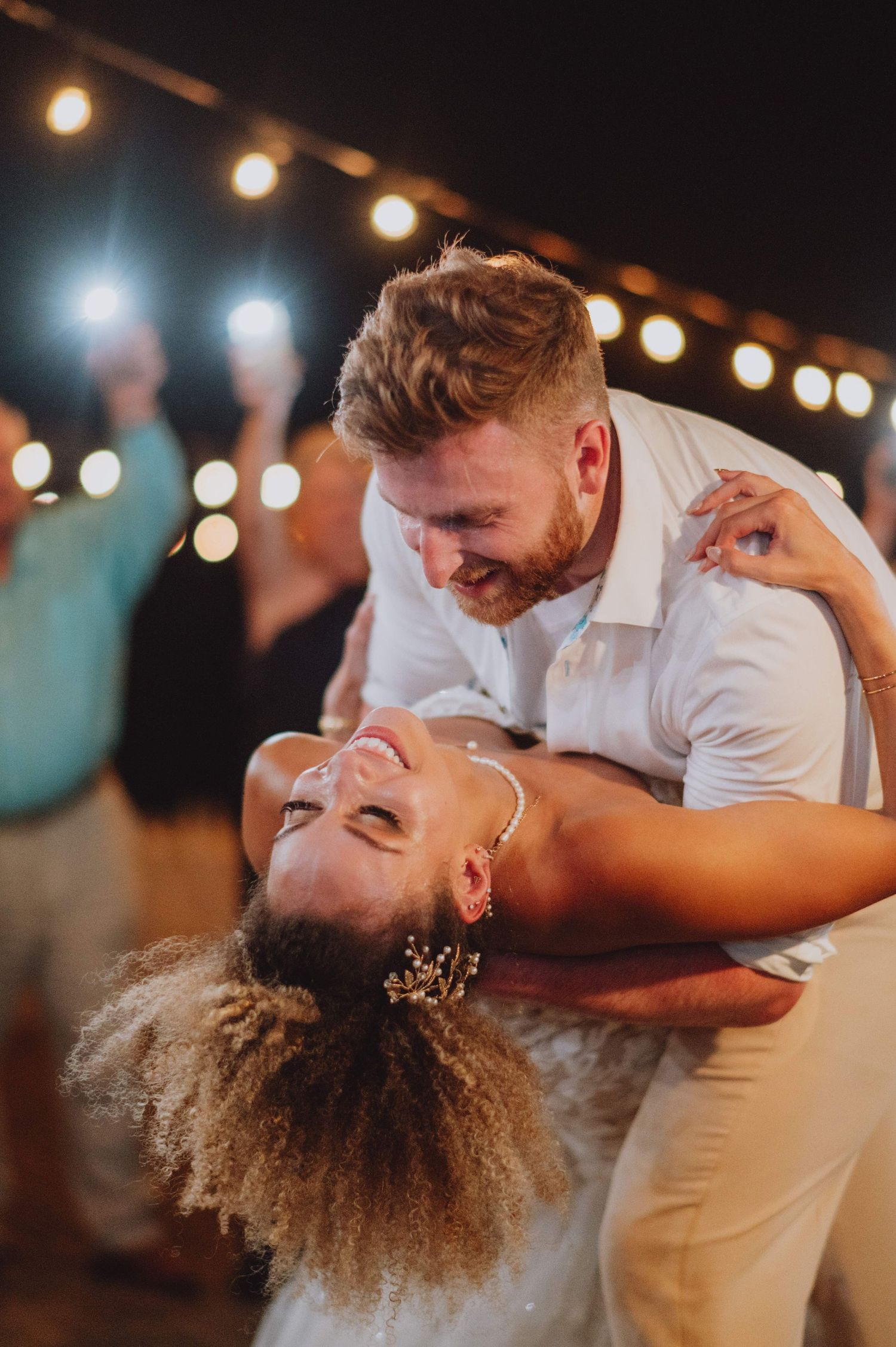 Couple performs romantic dance dip during evening wedding reception under string lights.