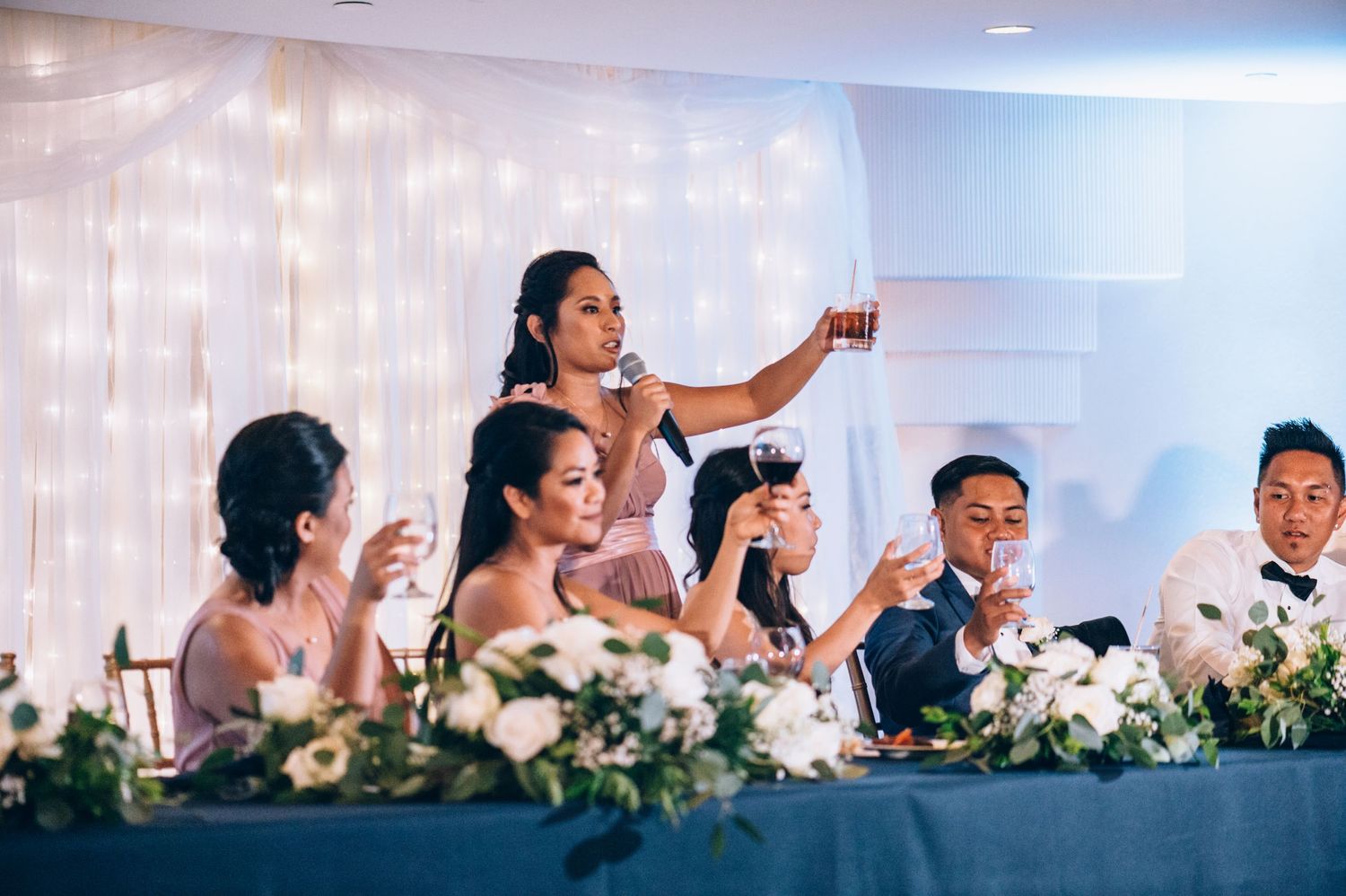 Wedding reception venue with elegant white floral decorations and twinkle light backdrop.