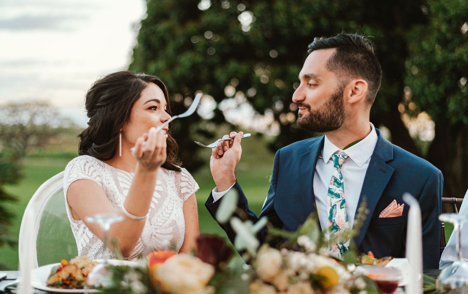 Couple sharing a lighthearted moment feeding each other at their outdoor wedding reception.