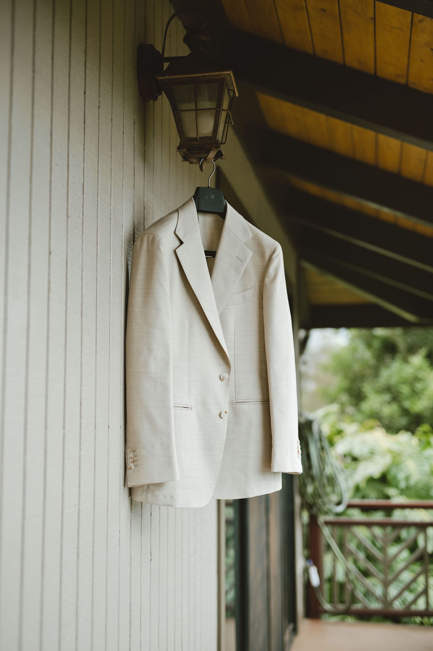 White blazer hanging on a hanger from a wall lamp on a wooden porch, perfect for a wedding or formal event.