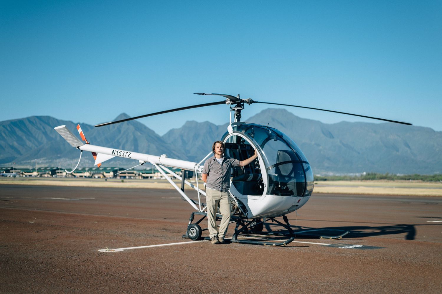 A helicopter parked on a desert airfield with mountains in the background.