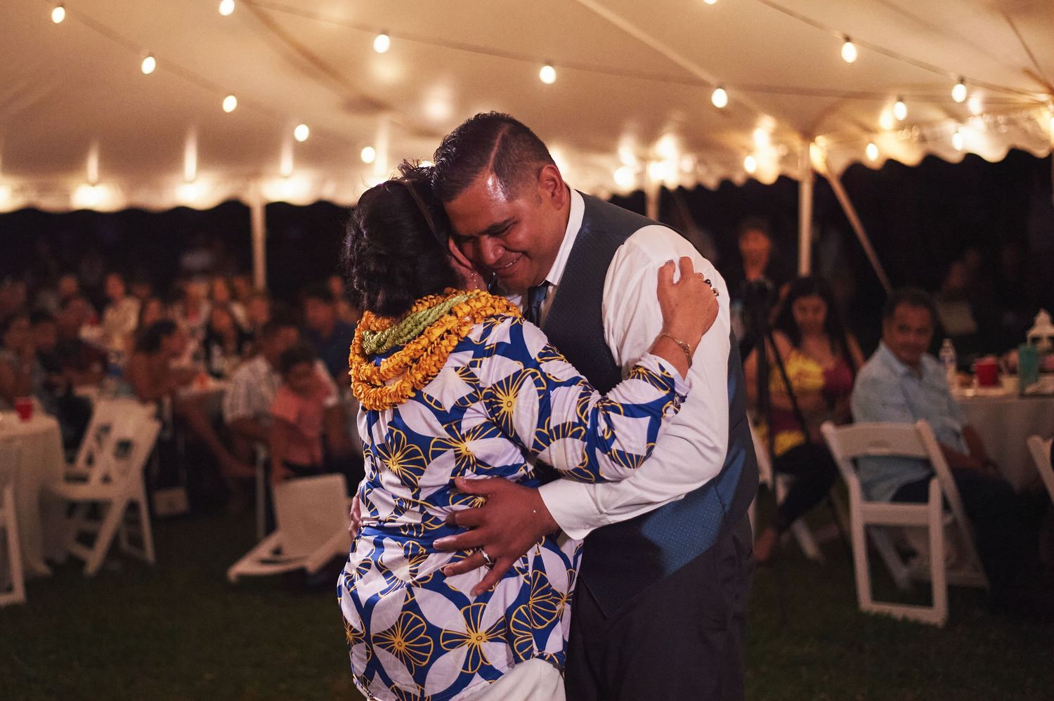 A tender dance moment at a wedding reception under a tent with string lights.