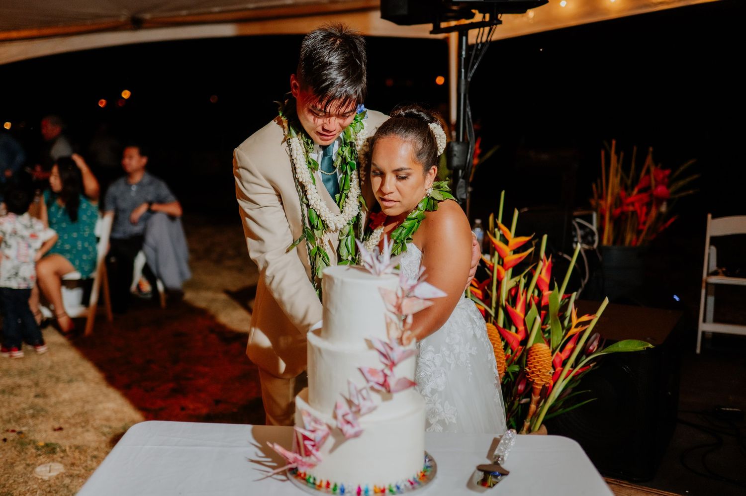 Newlyweds cutting their white wedding cake decorated with tropical flowers.