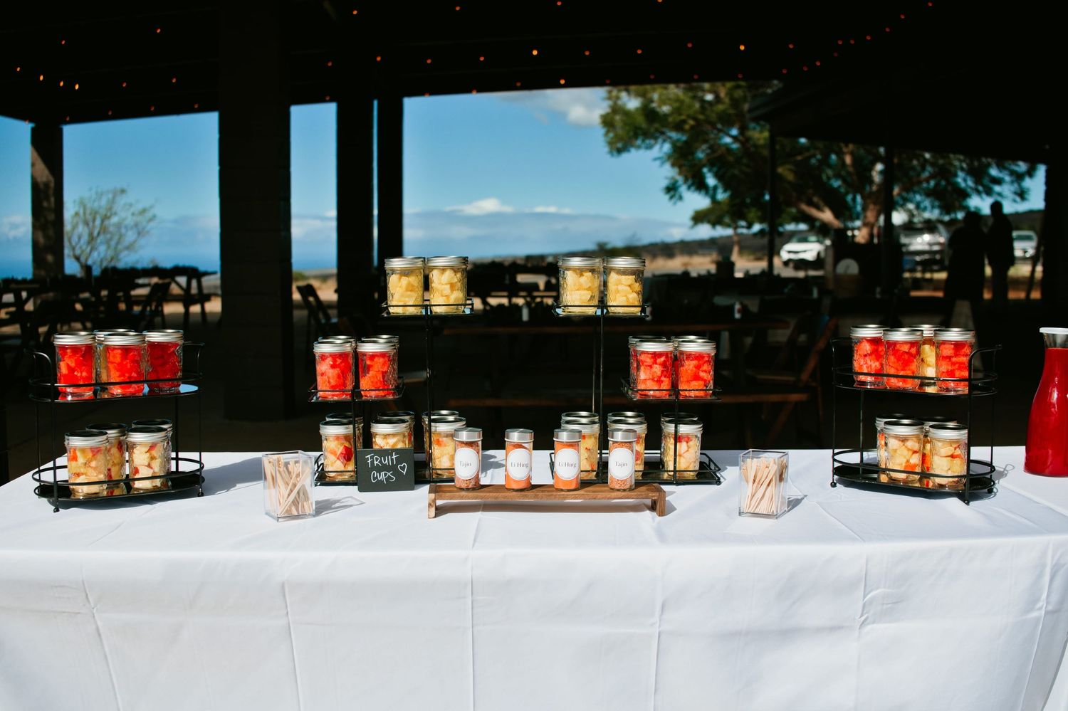 Mason jar display on white tablecloth at outdoor wedding reception with scenic ocean view backdrop.