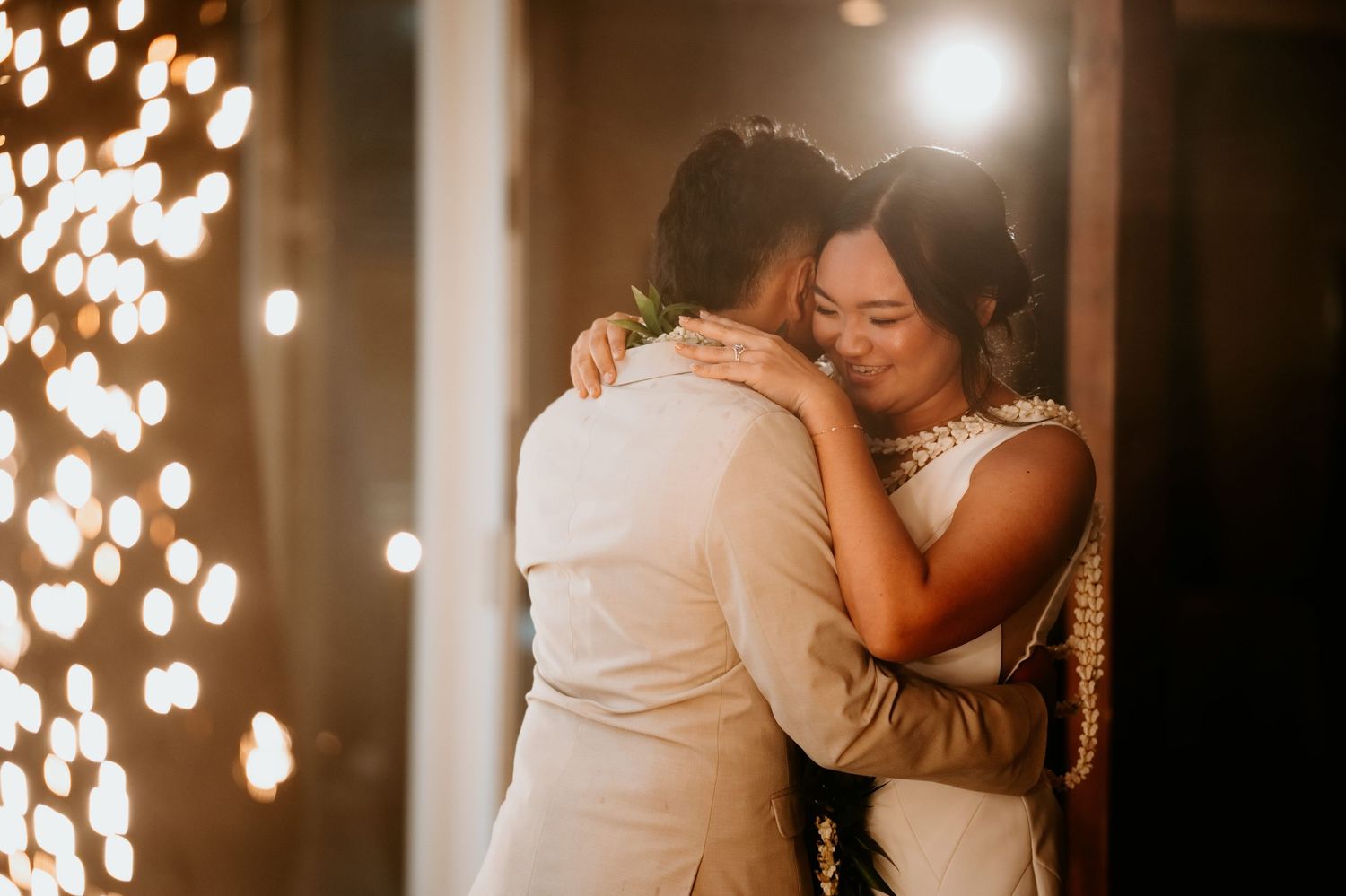 Bride and groom share an emotional embrace during their first dance, surrounded by warm bokeh string lights.