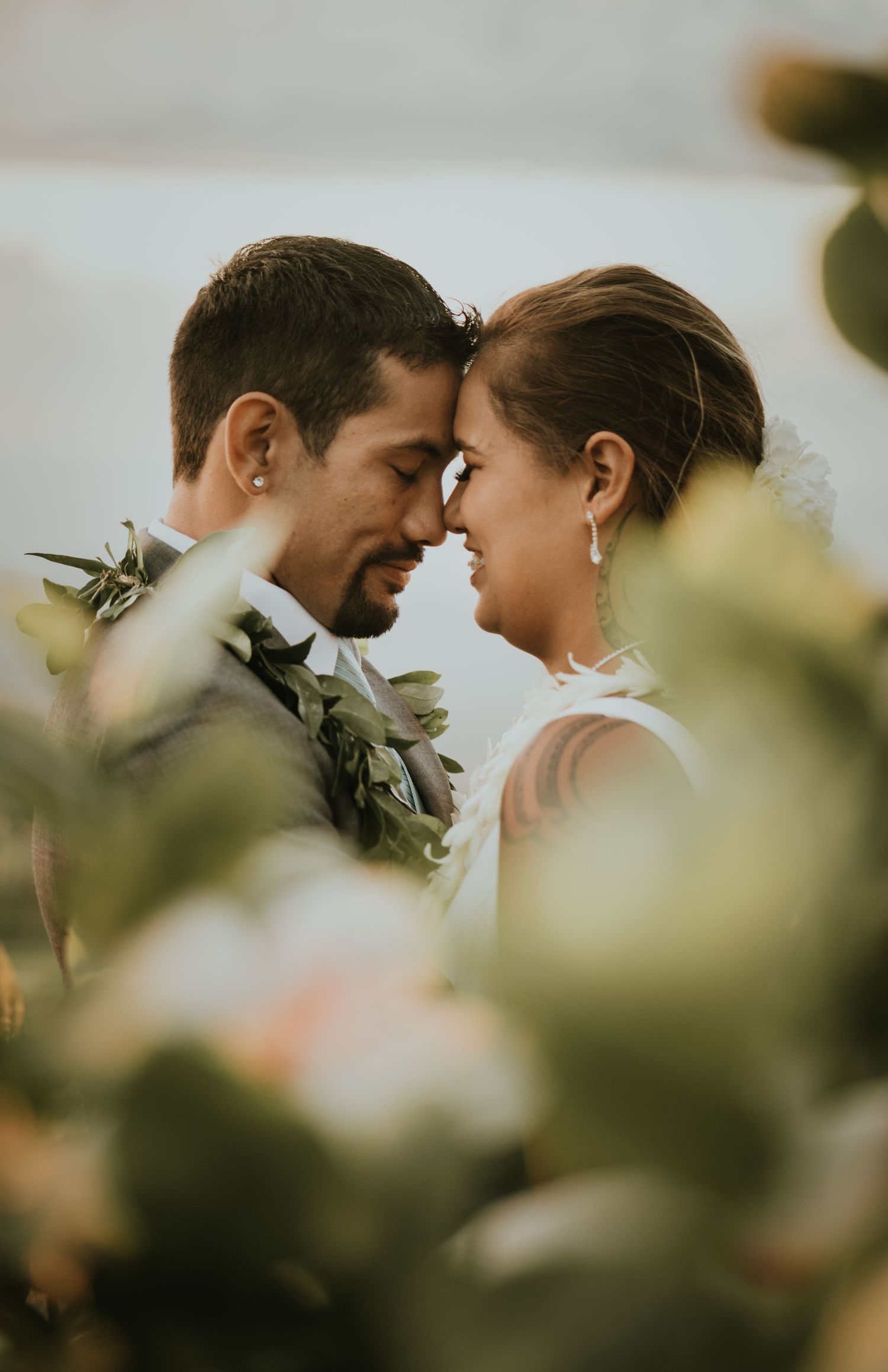 Intimate close-up portrait of a couple wearing green leaf leis against blurred foliage.