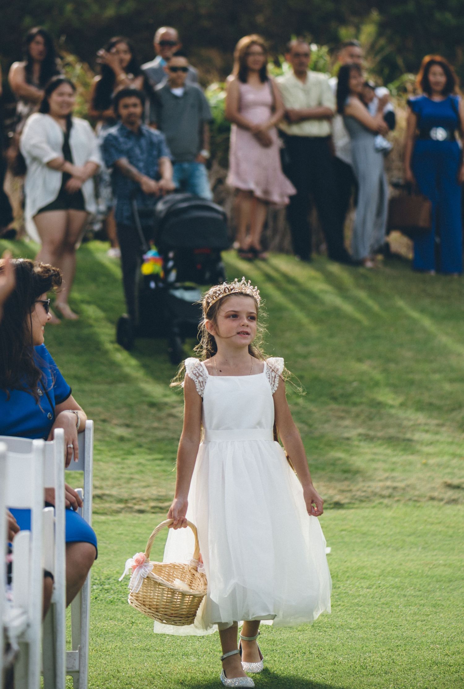 Young flower girls in white dresses walking down the aisle carrying baskets.