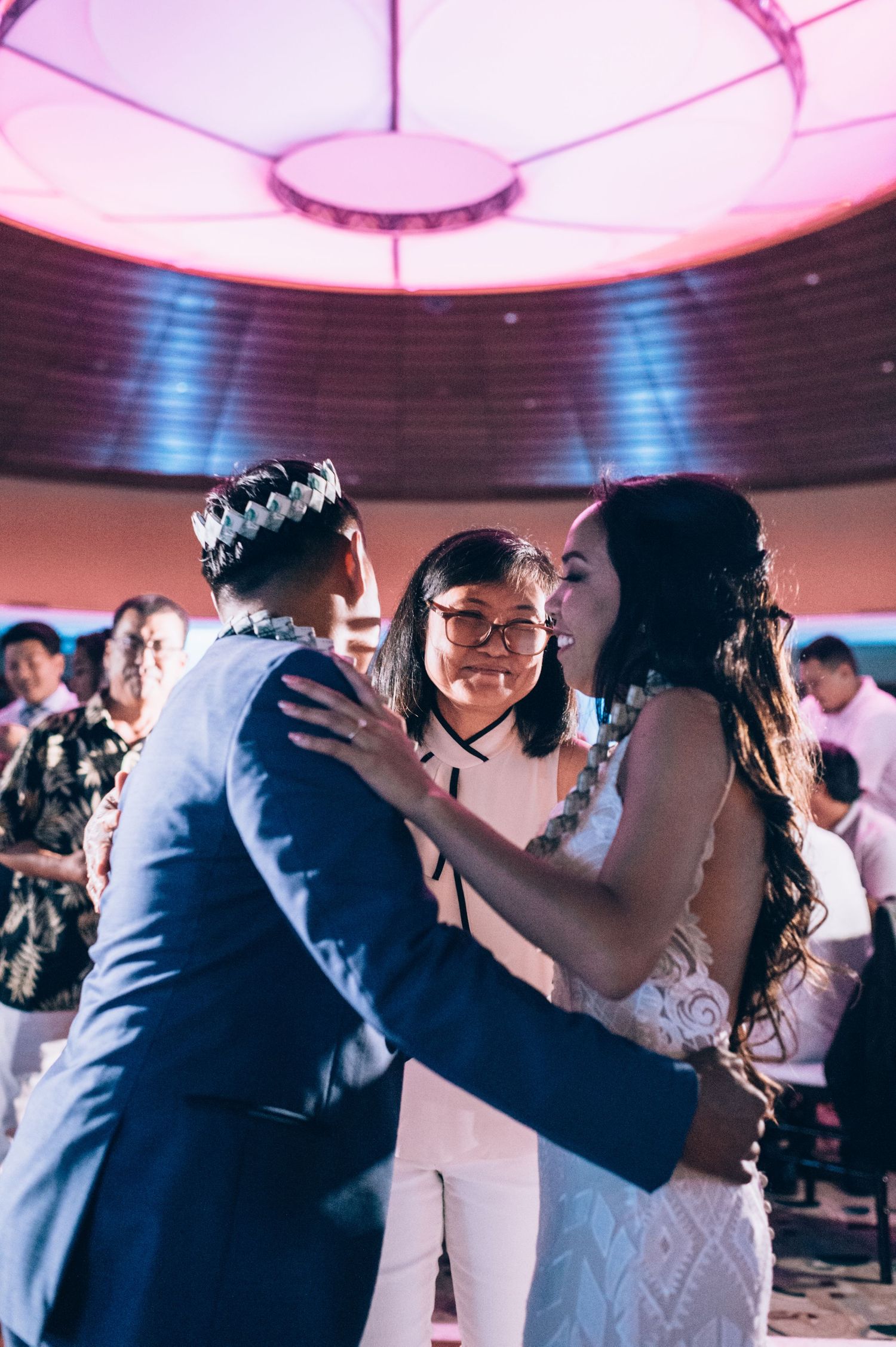 Couples dance together at a wedding reception under pink lighting in an elegant ballroom setting.