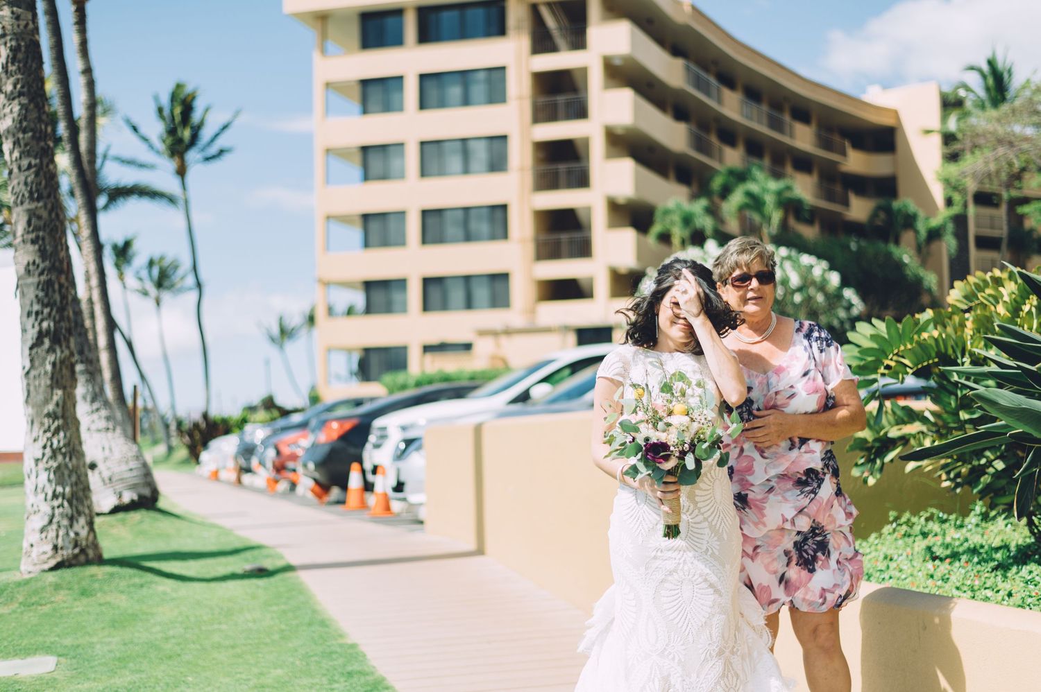 Beachside wedding moment captured with resort buildings and palm trees in background.