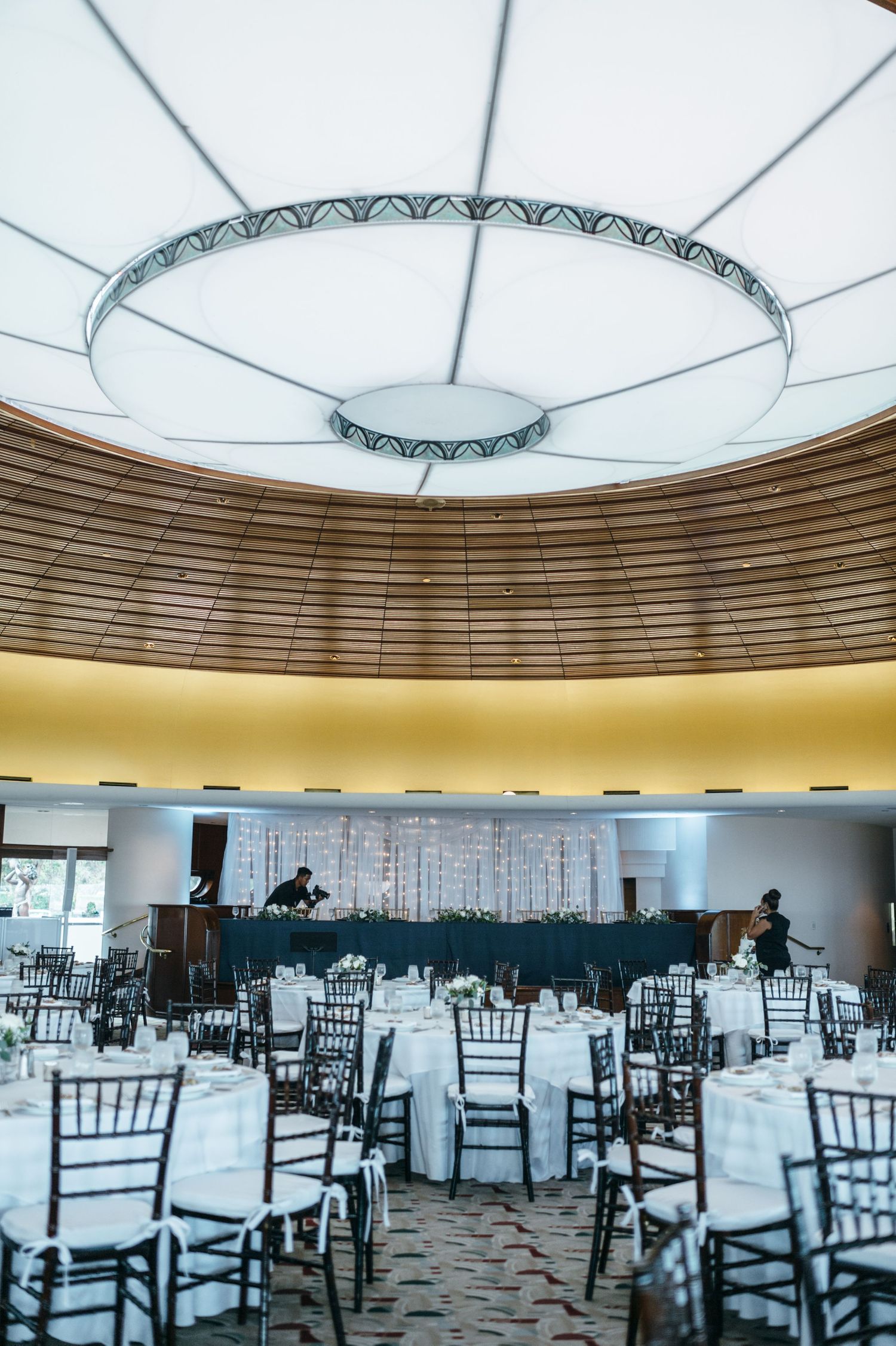 Modern wedding venue with geometric ceiling design and black chiavari chairs.