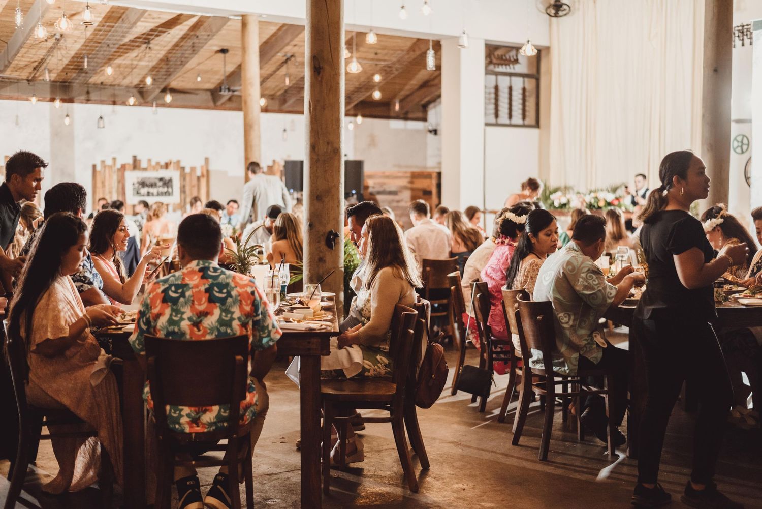Wedding reception guests mingling in a rustic wooden barn venue with warm lighting.