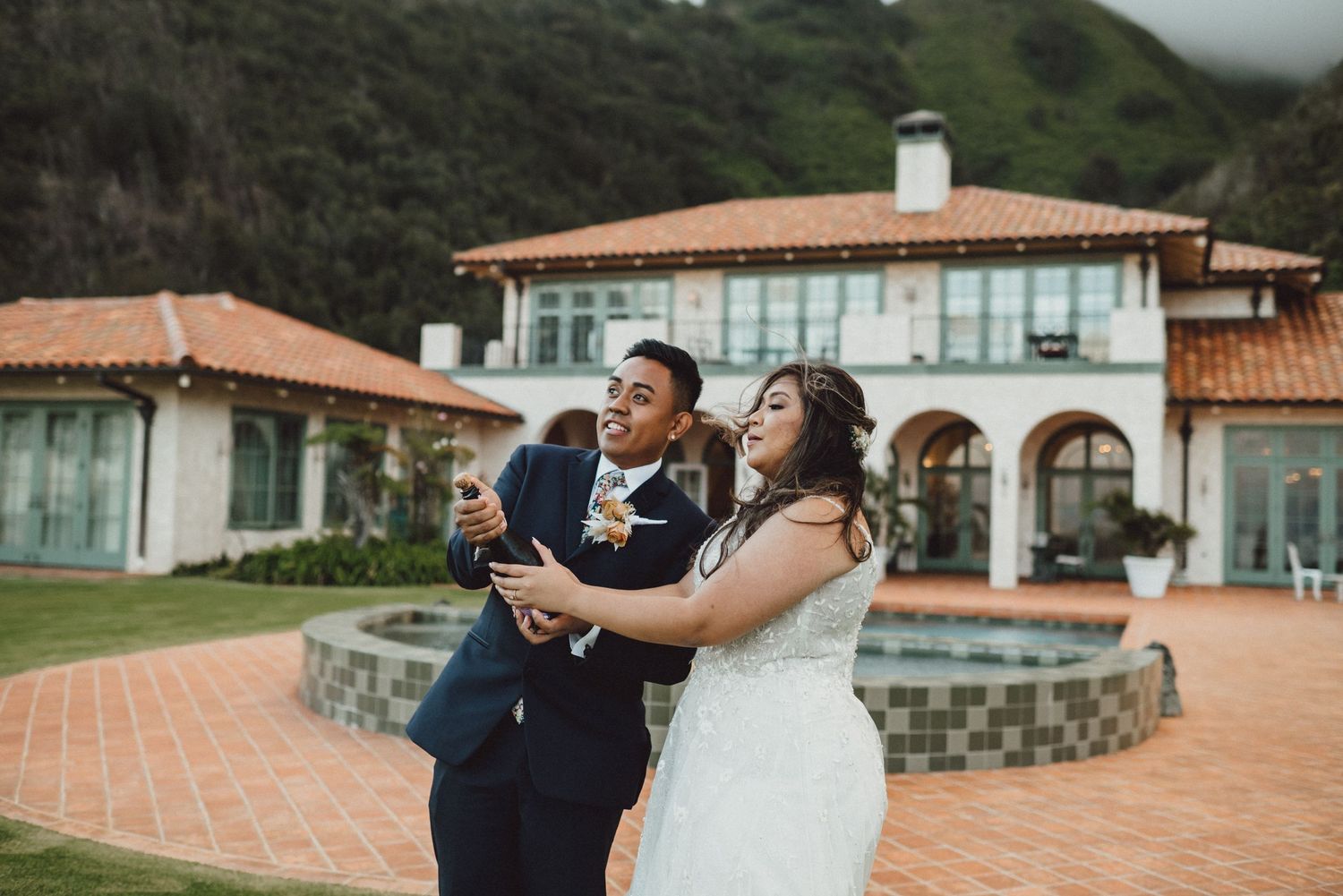 A couple in wedding attire shares a joyful moment by a pool at a Mediterranean villa.
