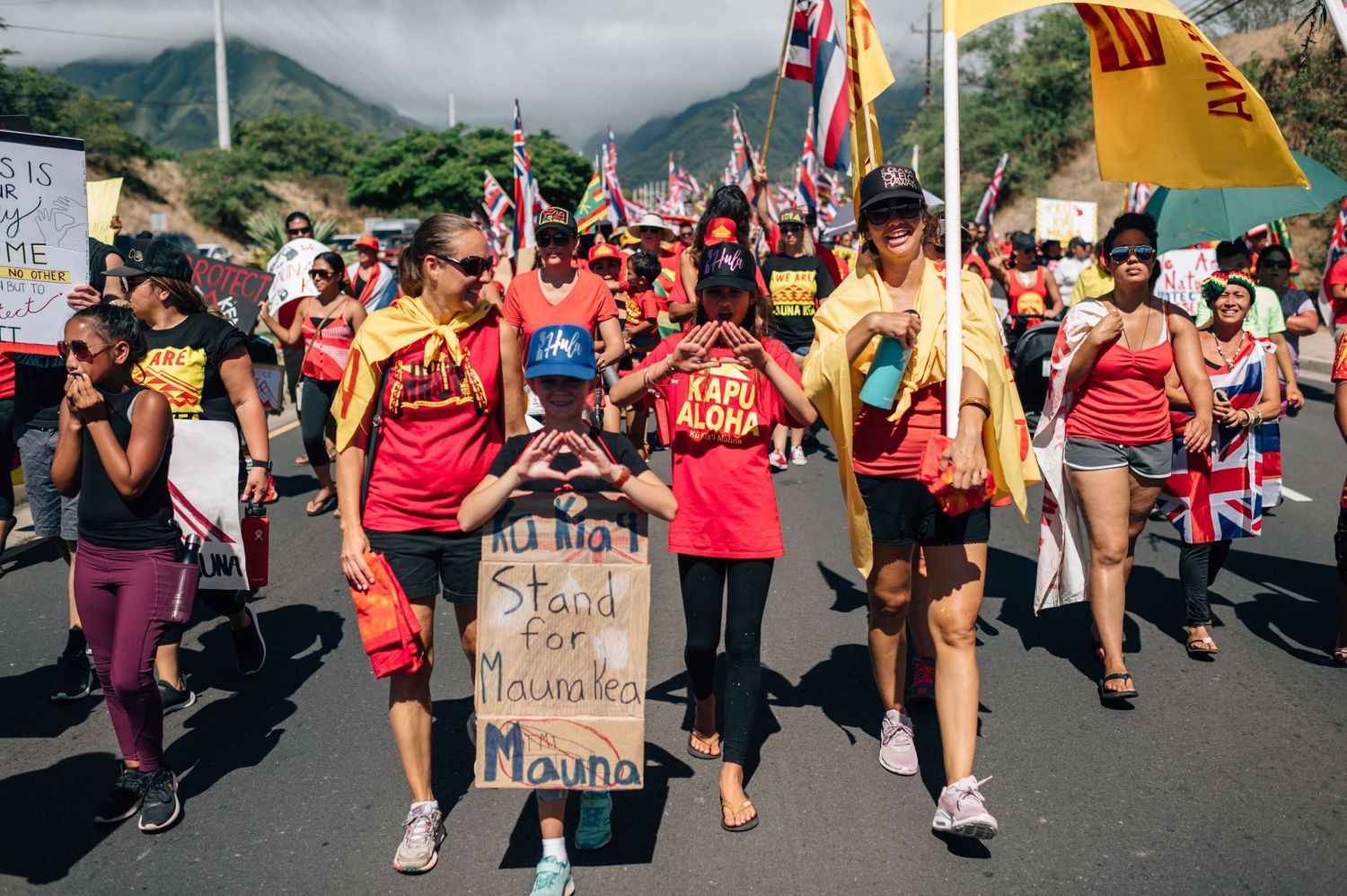 Protesters march with signs and flags along a mountain road during demonstration.