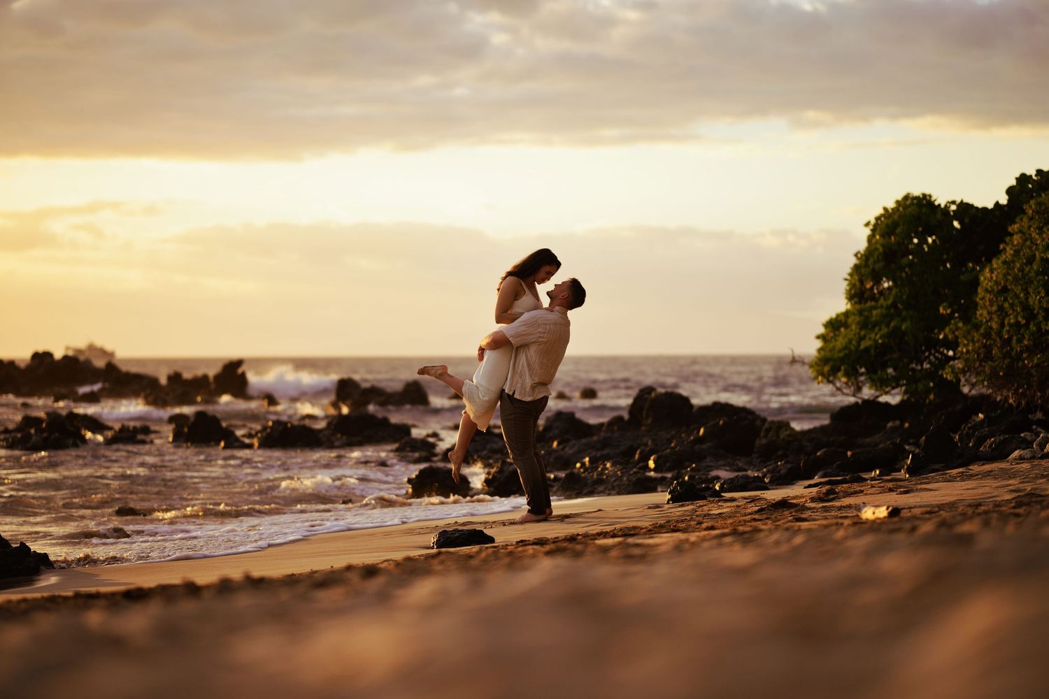 Couple embracing on a rocky beach at golden sunset in Maui Hawaii.