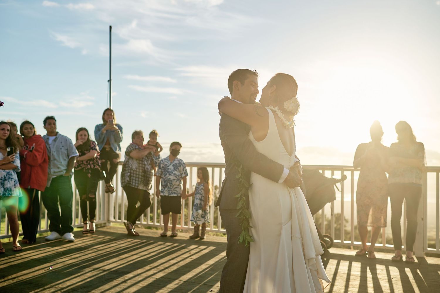 Silhouettes of wedding guests gathered on a deck during golden hour sunset.