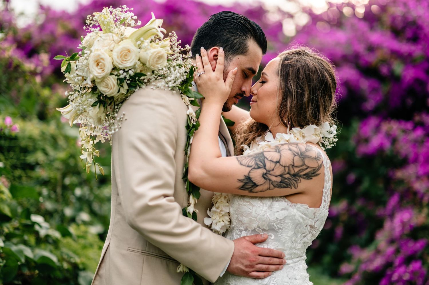 Romantic wedding couple embraces among vibrant purple bougainvillea flowers.
