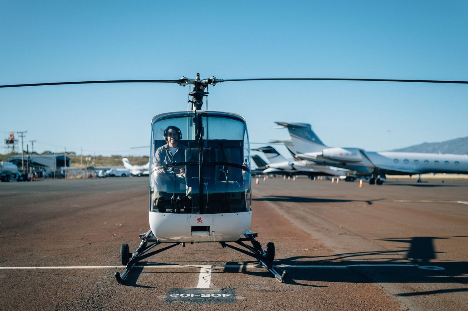 White helicopter parked on desert airfield with mountains in background.