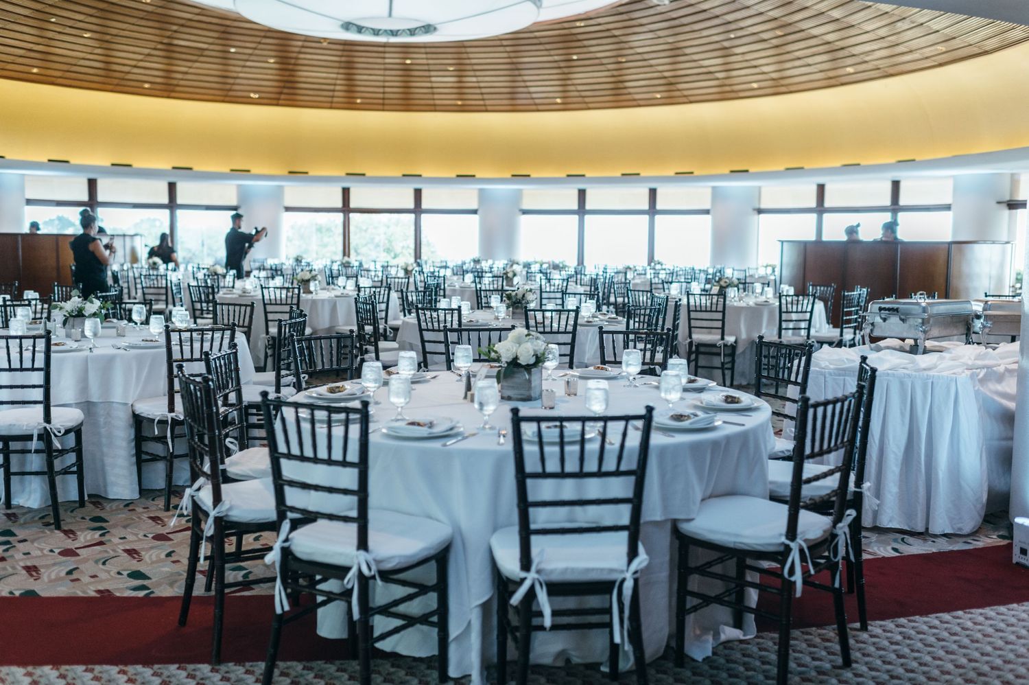 Spacious wedding reception venue with white tablecloths and black chiavari chairs.