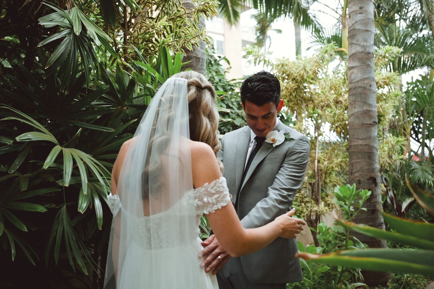 Bride and groom share an intimate moment surrounded by lush tropical greenery during outdoor wedding ceremony.