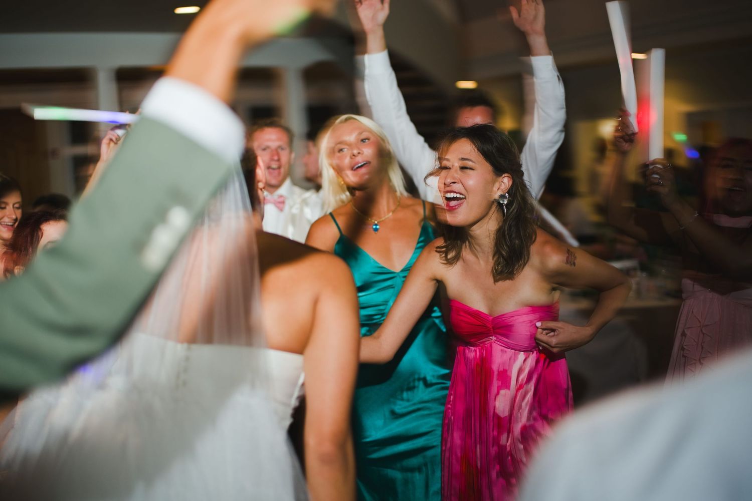 Guests dancing joyfully at a wedding reception, women in teal and pink dresses celebrating on the dance floor.