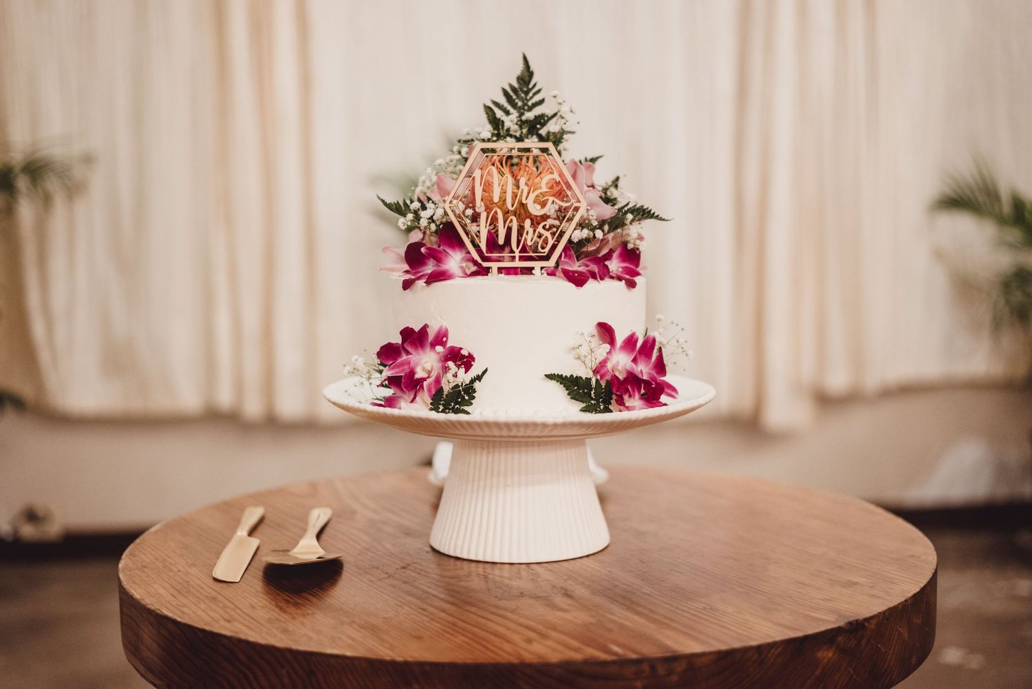 Elegant white wedding cake displayed on wooden table with pink floral decorations.