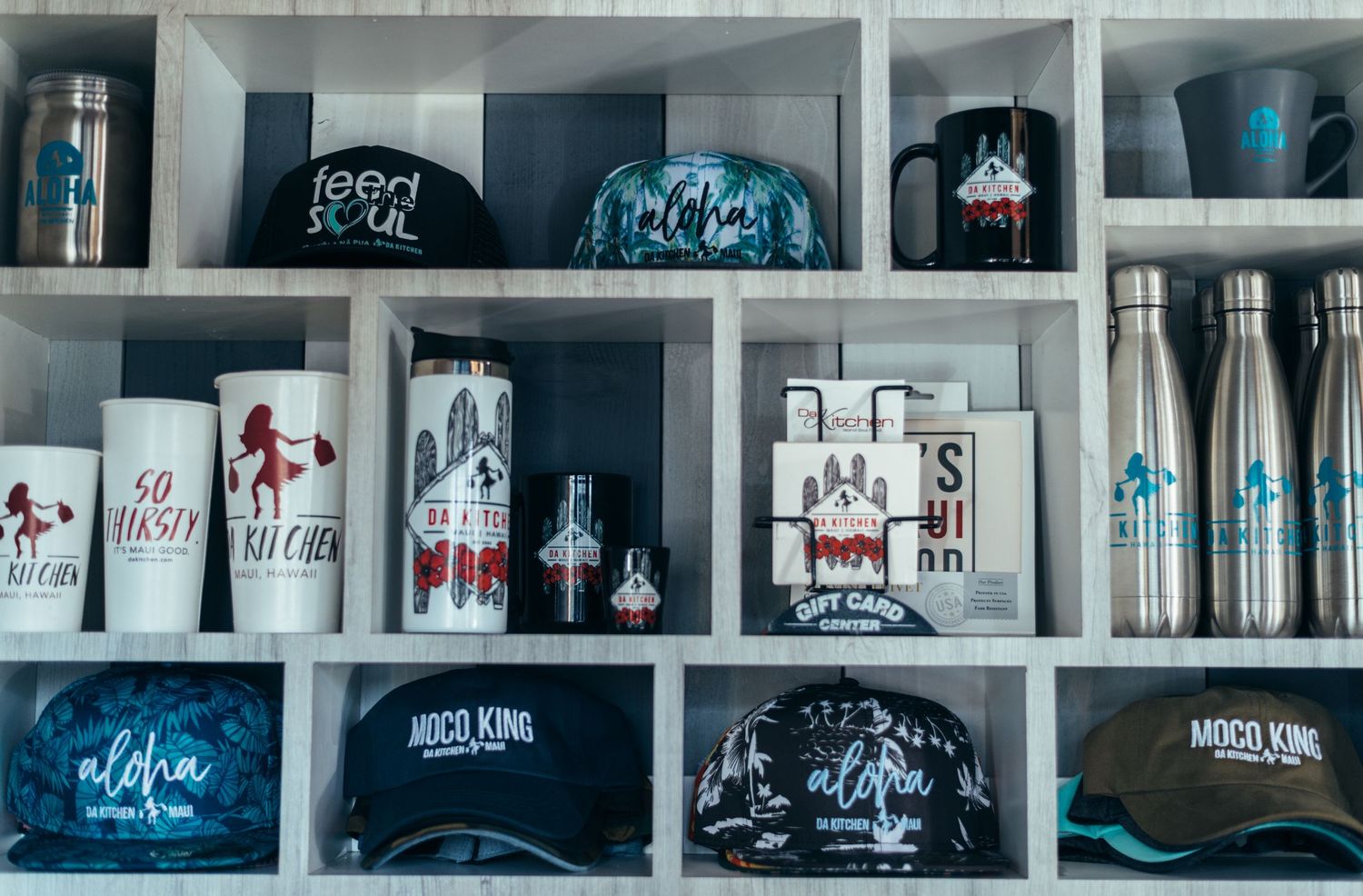 Retail display shelf with branded merchandise including hats, cups, and water bottles.