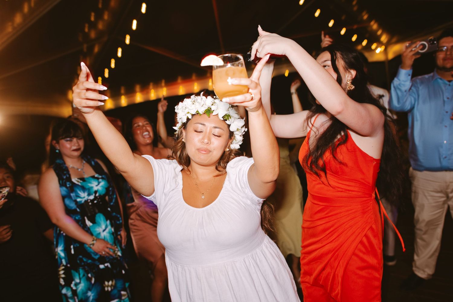 Bride wearing flower crown dancing joyfully with guests at an outdoor wedding reception.