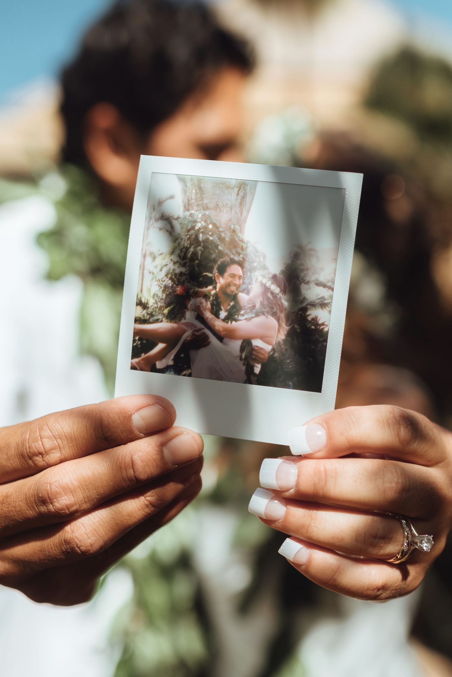 Couple holding Polaroid photo of their joyful Maui wedding ceremony outdoors.