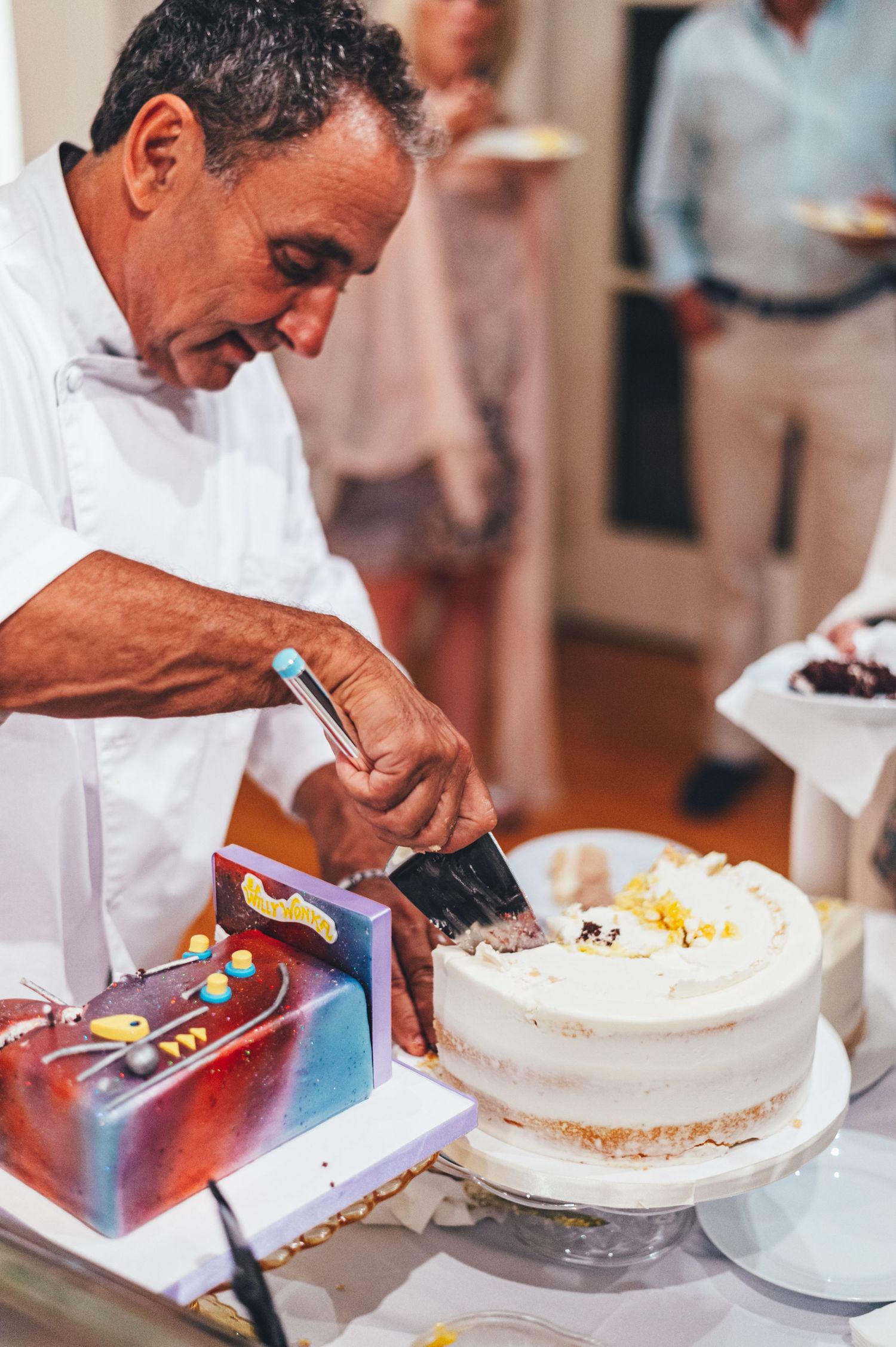 Chef in white uniform carefully cutting and plating pieces of wedding cake.