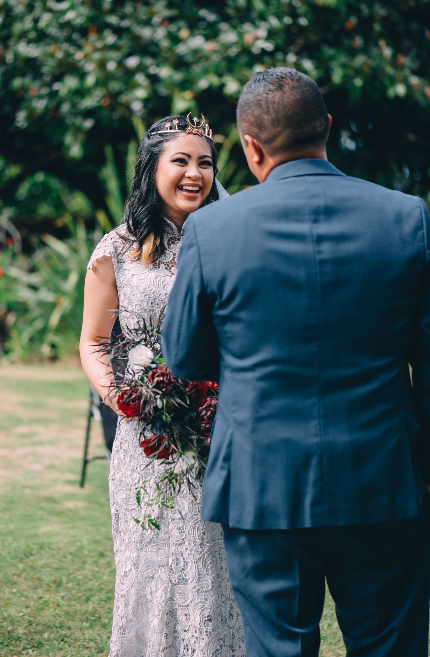 Couple exchanging vows during outdoor wedding ceremony with lush greenery backdrop.