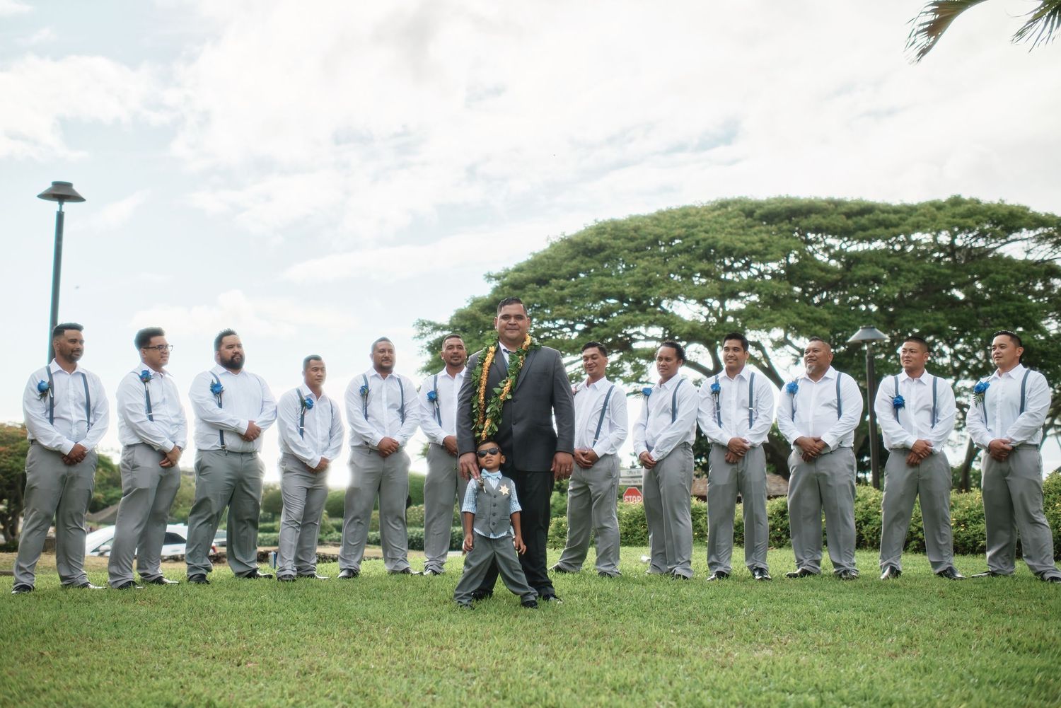 Wedding party members in gray suits pose in various formations on a grassy hillside.