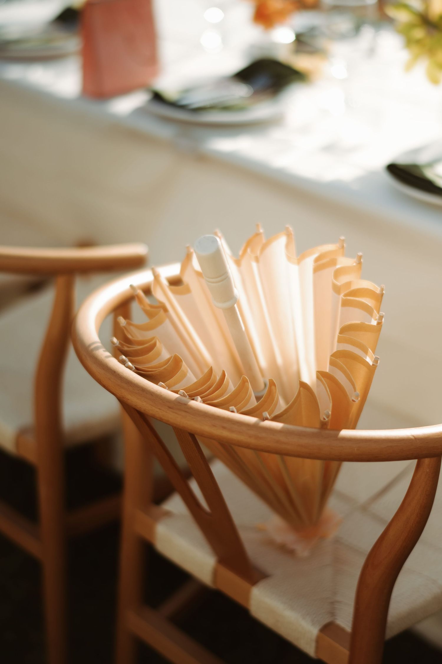 Elegant wooden wishbone chairs holding folded paper fans at a wedding reception table setting.