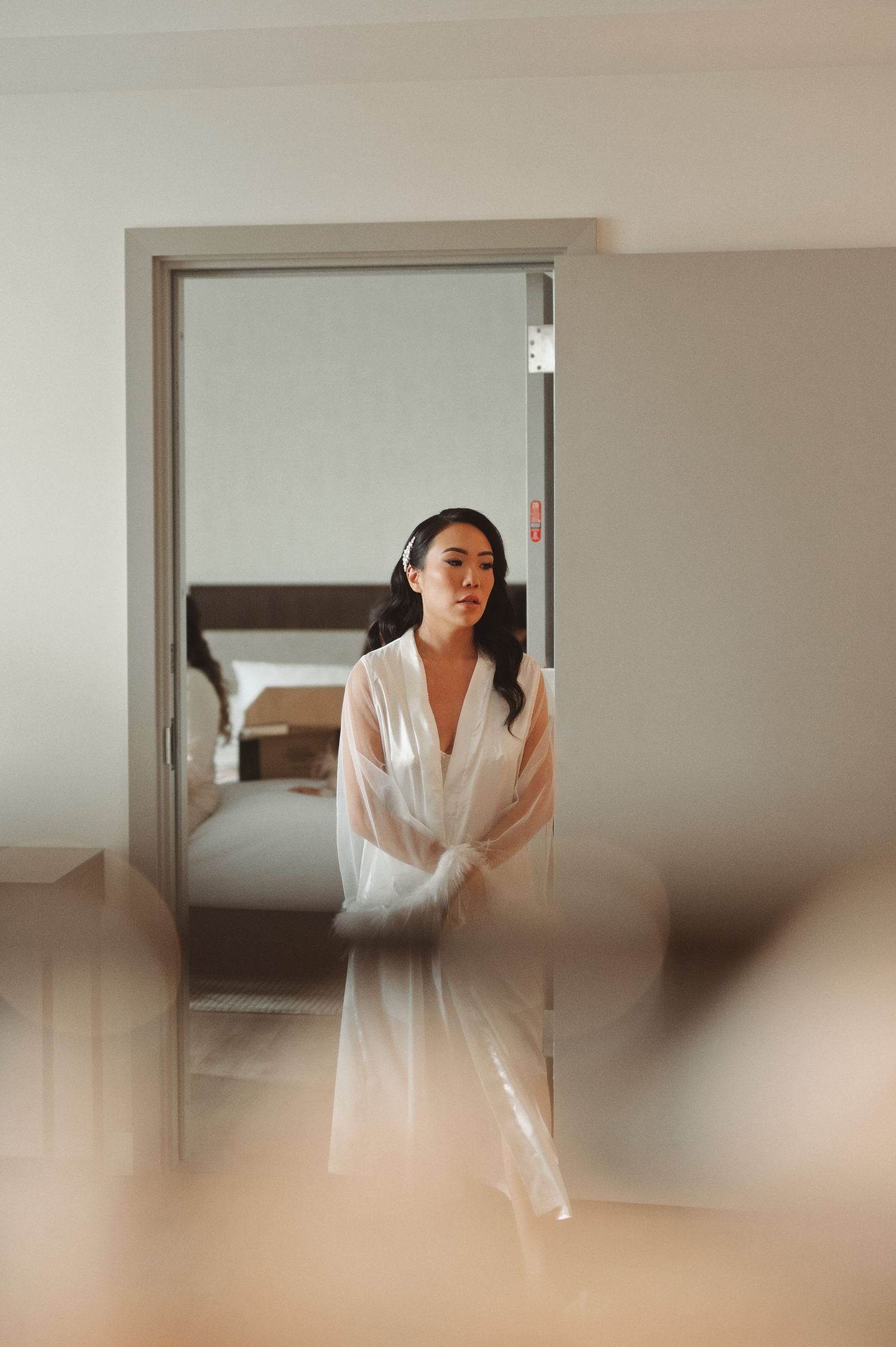 A bride in a white sheer robe stands in a doorway, looking serene before her wedding ceremony.
