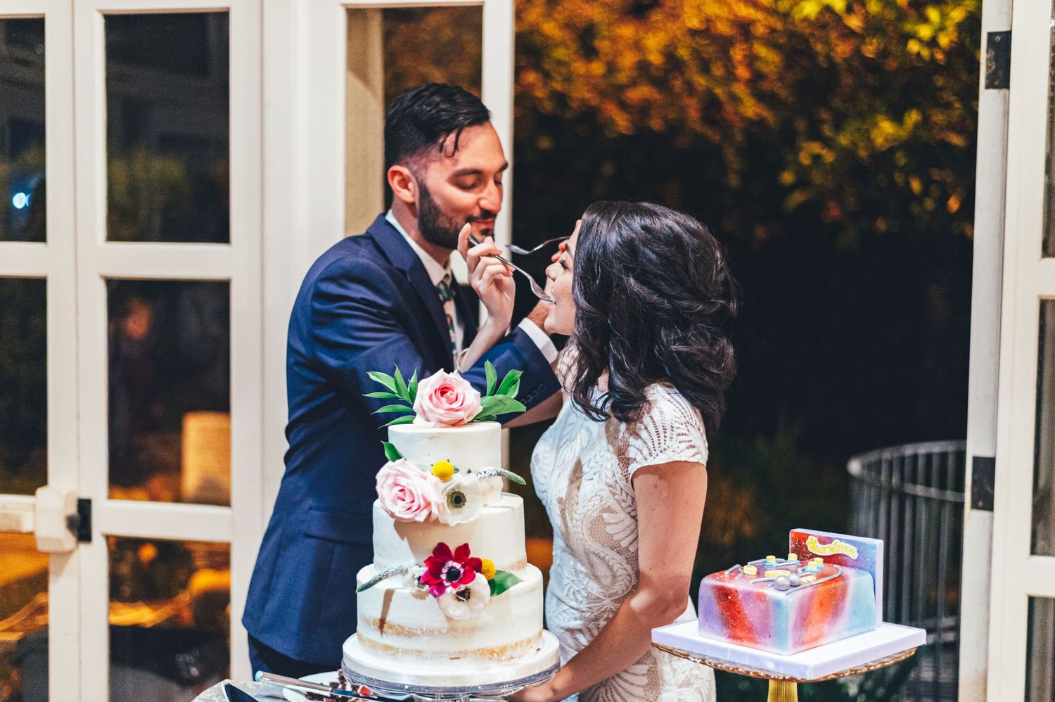 Wedding couple sharing cake during their reception with autumn foliage in background.
