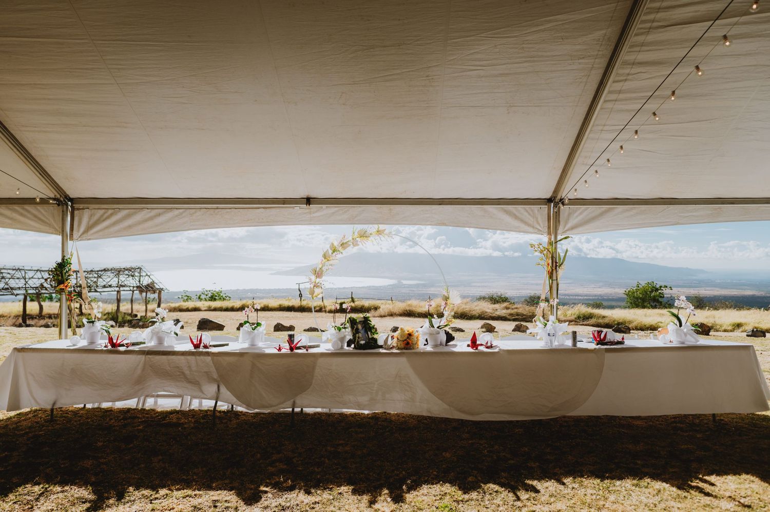 Wedding reception tables set up under a white tent with ocean views in the background.