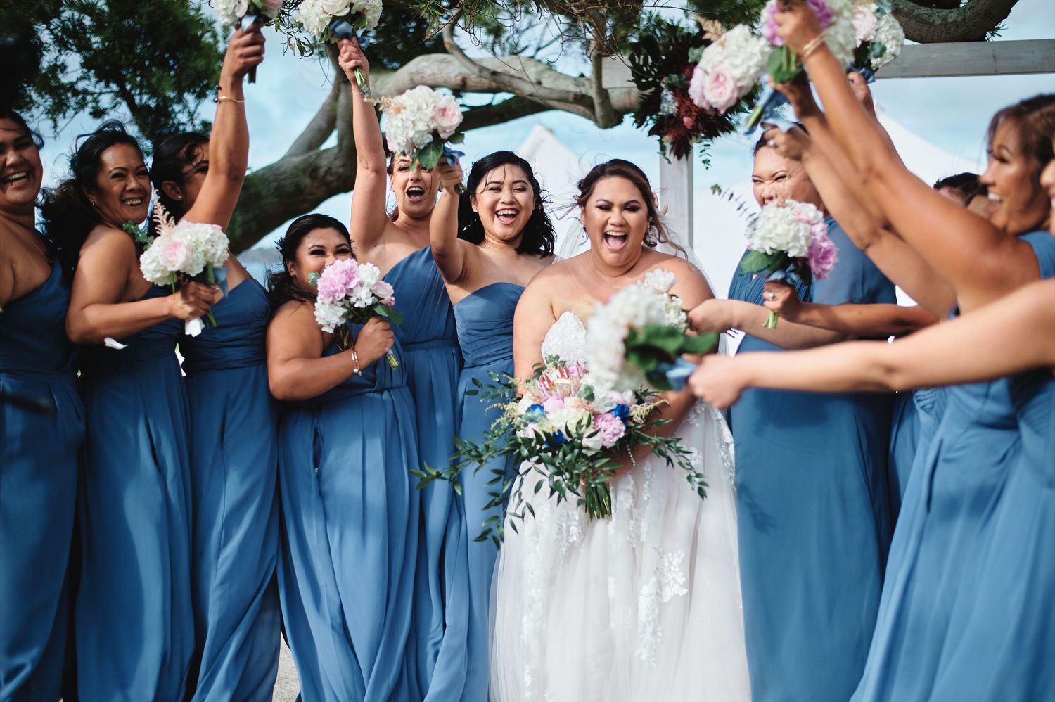 Wedding party in coordinated blue dresses and formal attire poses together outdoors.
