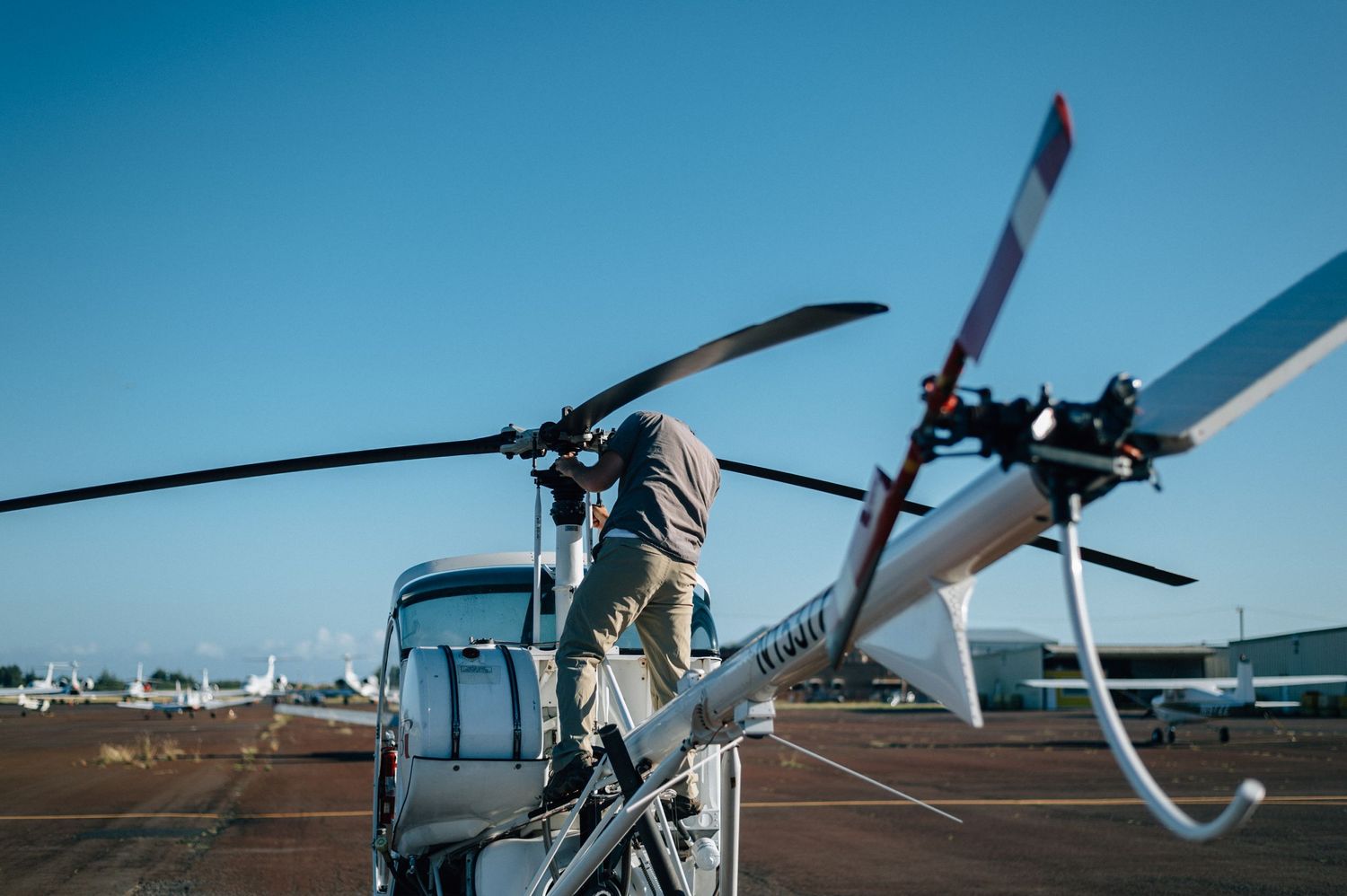 Helicopter maintenance inspection being performed on tarmac with other aircraft visible.