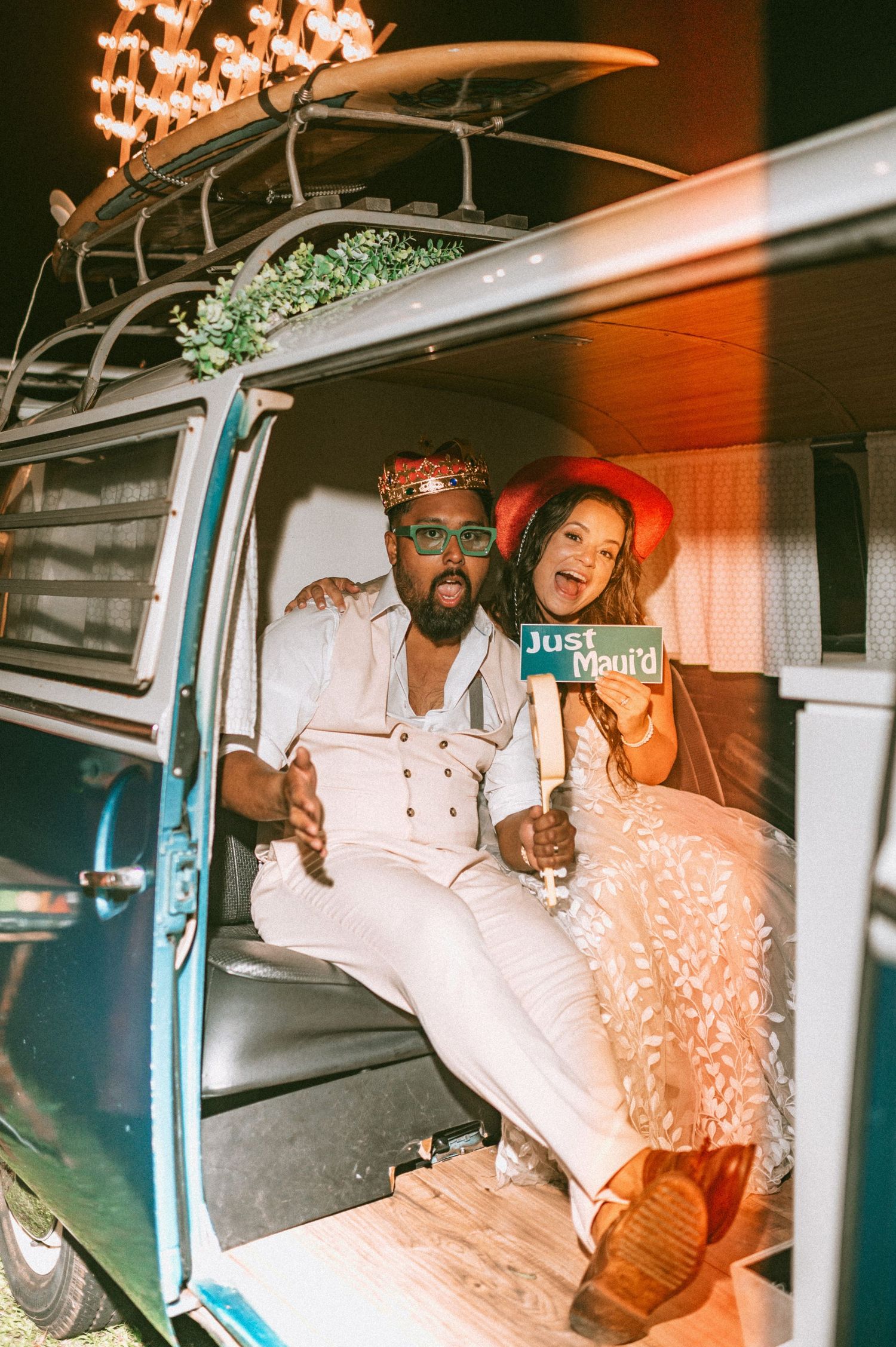 Newlyweds celebrate inside a vintage VW bus holding a Just Married sign at their fun wedding reception.