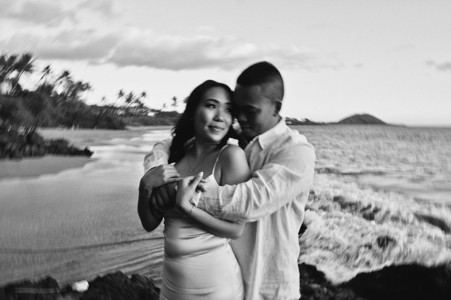 Couple sharing tender embrace on Hawaiian beach at sunset in black and white.
