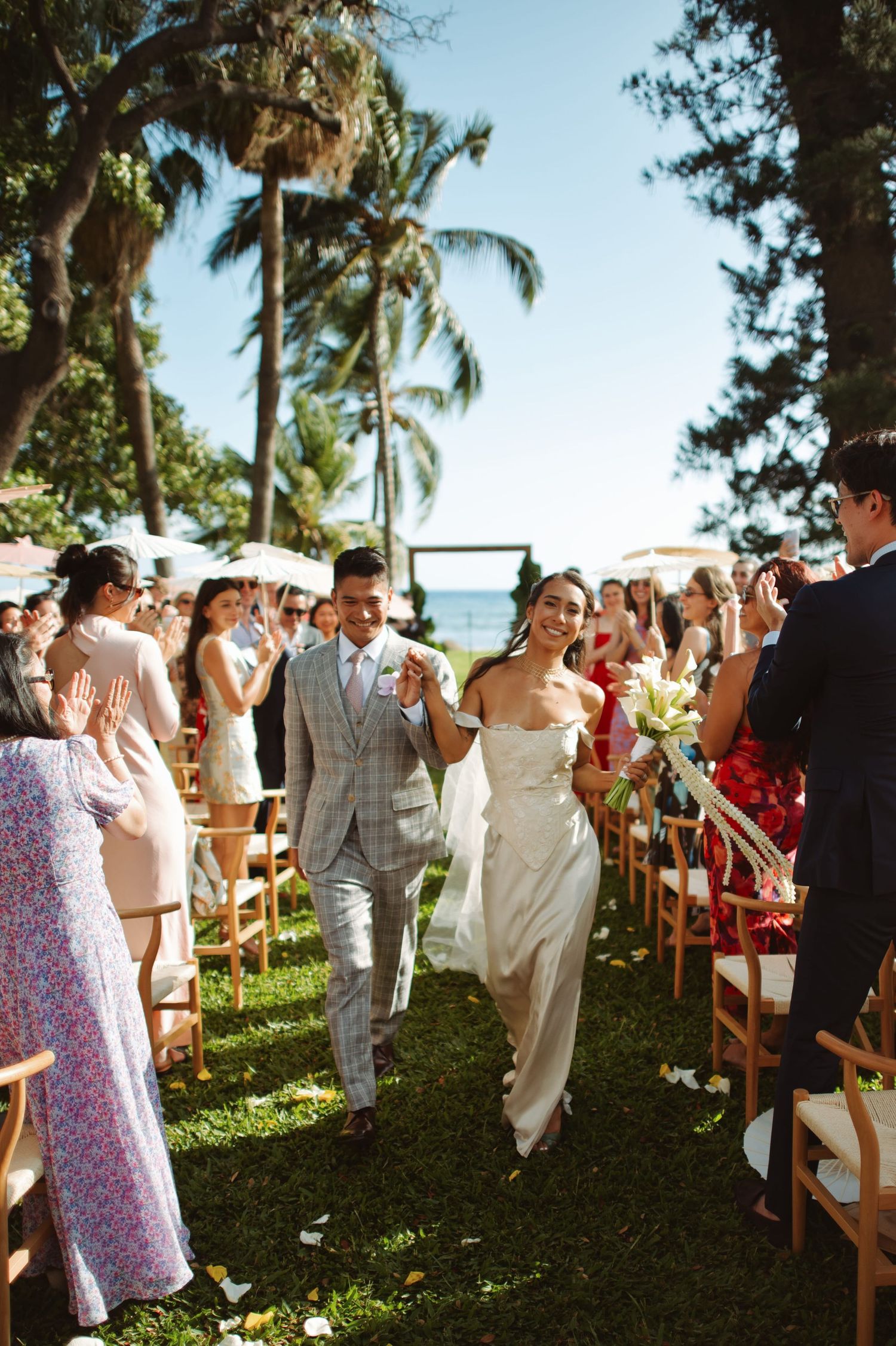 Joyful newlyweds walking down aisle at elegant outdoor Maui wedding ceremony by the ocean.