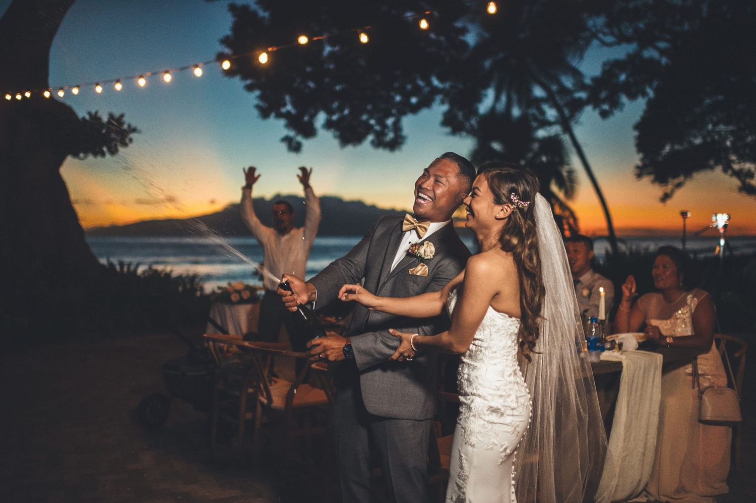 Bride and groom share a joyful first dance at a romantic outdoor beach wedding reception at sunset.