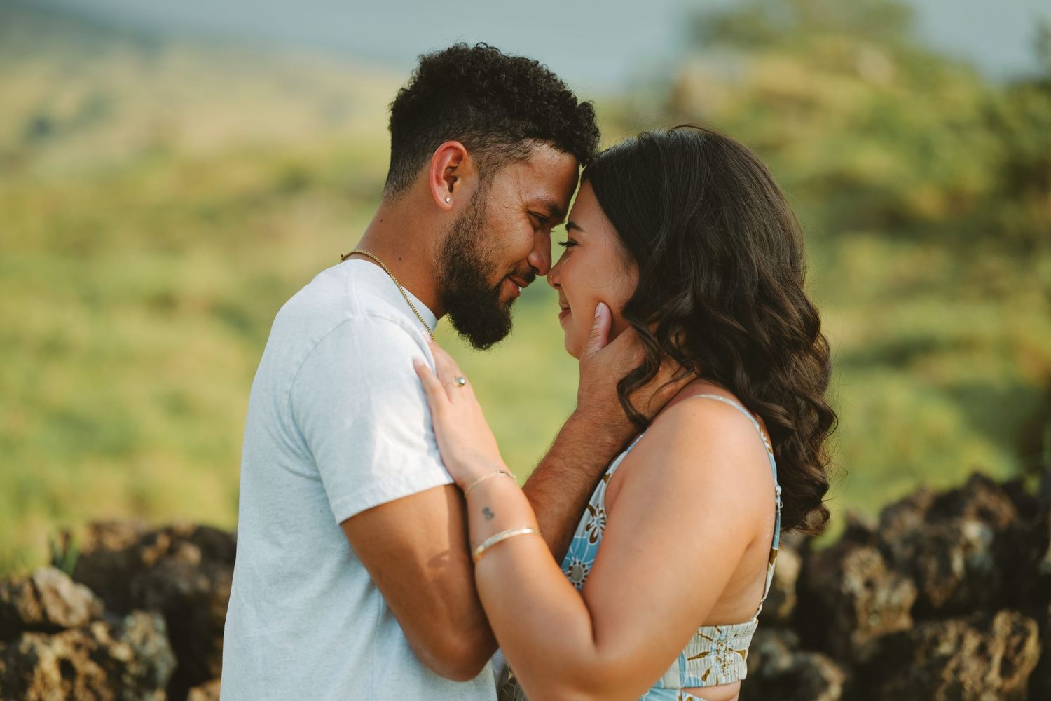 Romantic couple sharing an intimate moment outdoors with lush green hills in the background.