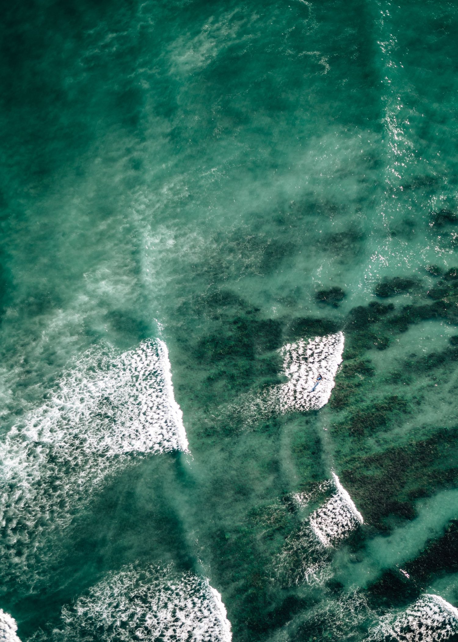 White foam patterns form geometric shapes in the turquoise ocean waters.