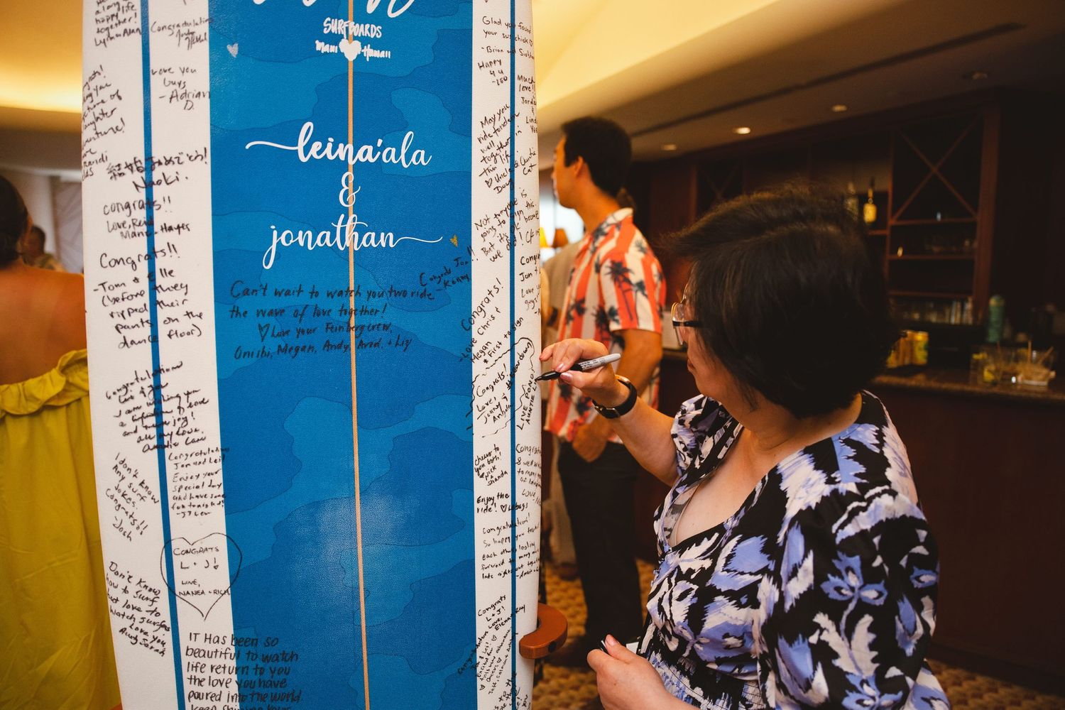 Guests signing a blue wedding guest book board with names Leinaala and Jonathan at a reception.